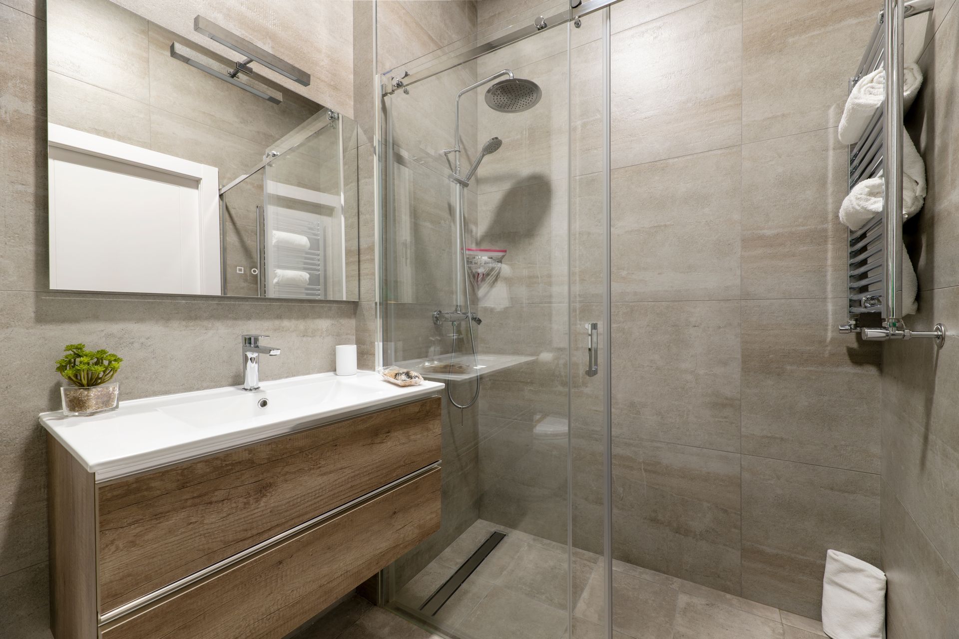 Modern beige bathroom with glass shower, wood vanity, large mirror, and towel rack