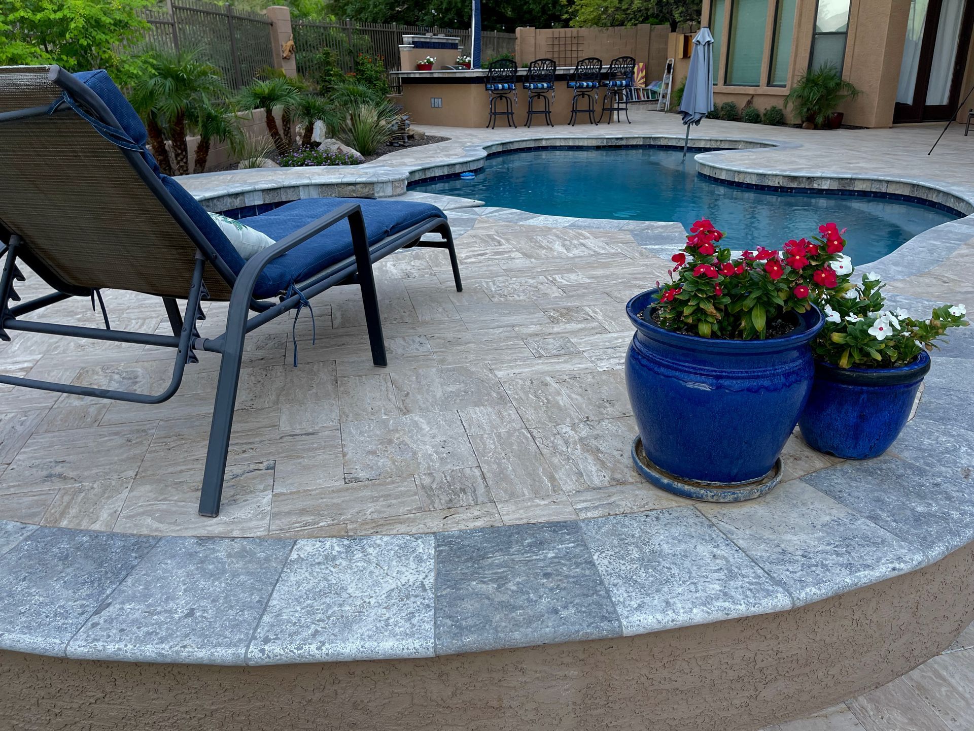 Patio lounge chair beside a pool with blue flower pots and red blooms