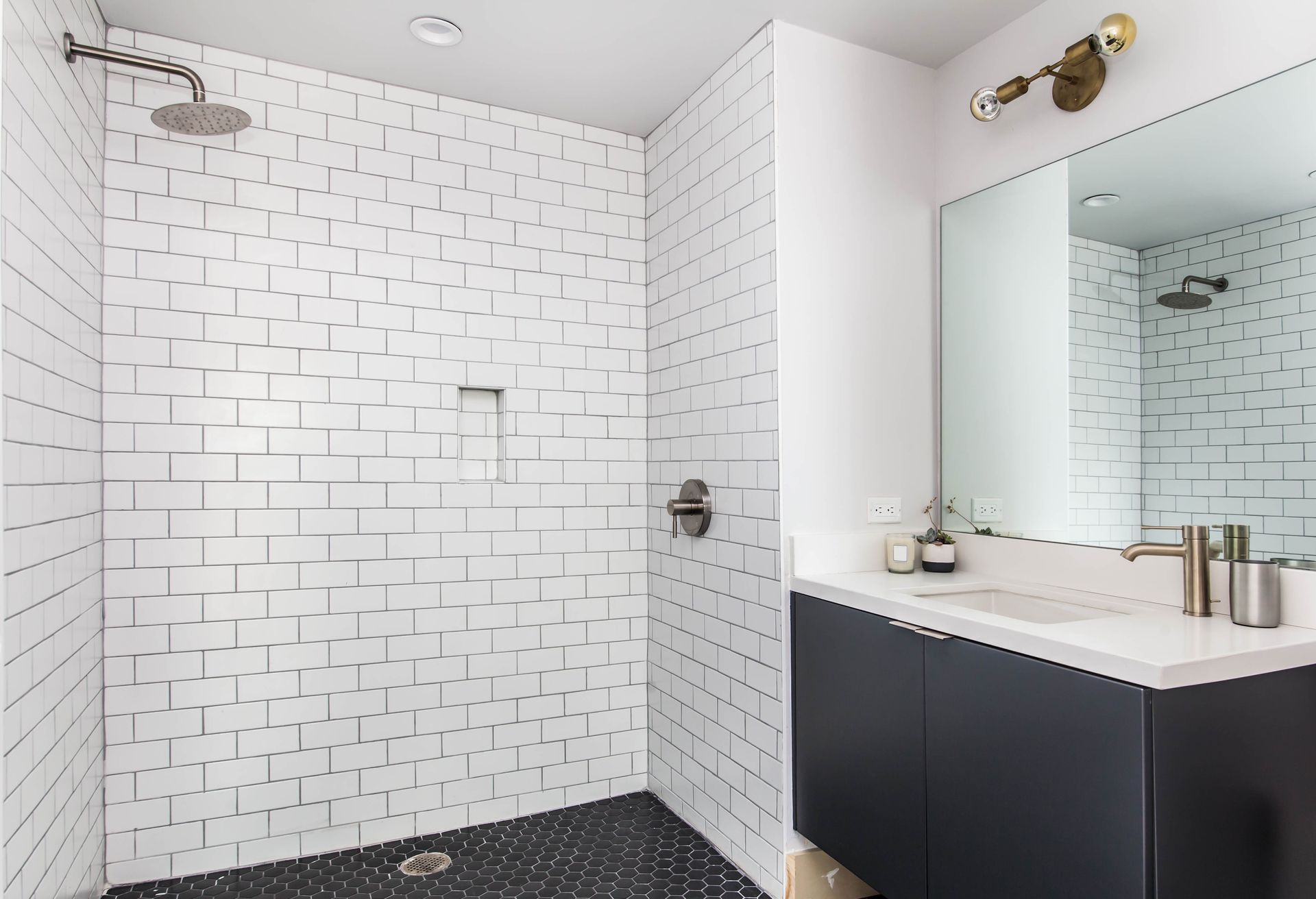 Modern white-tiled bathroom with walk-in shower, dark vanity, and large mirror