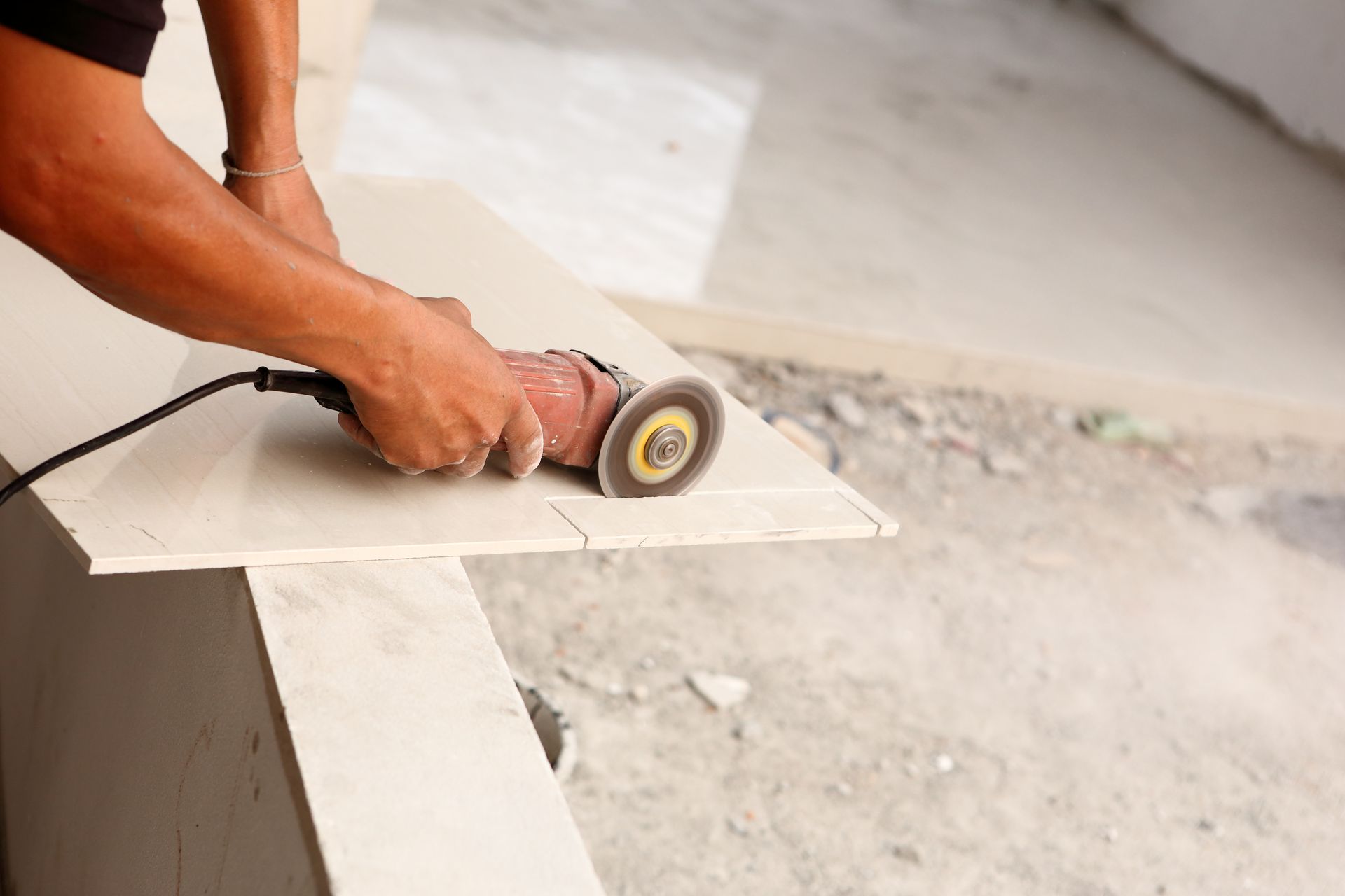 Hand using a power grinder to cut a white tile on a floor surface