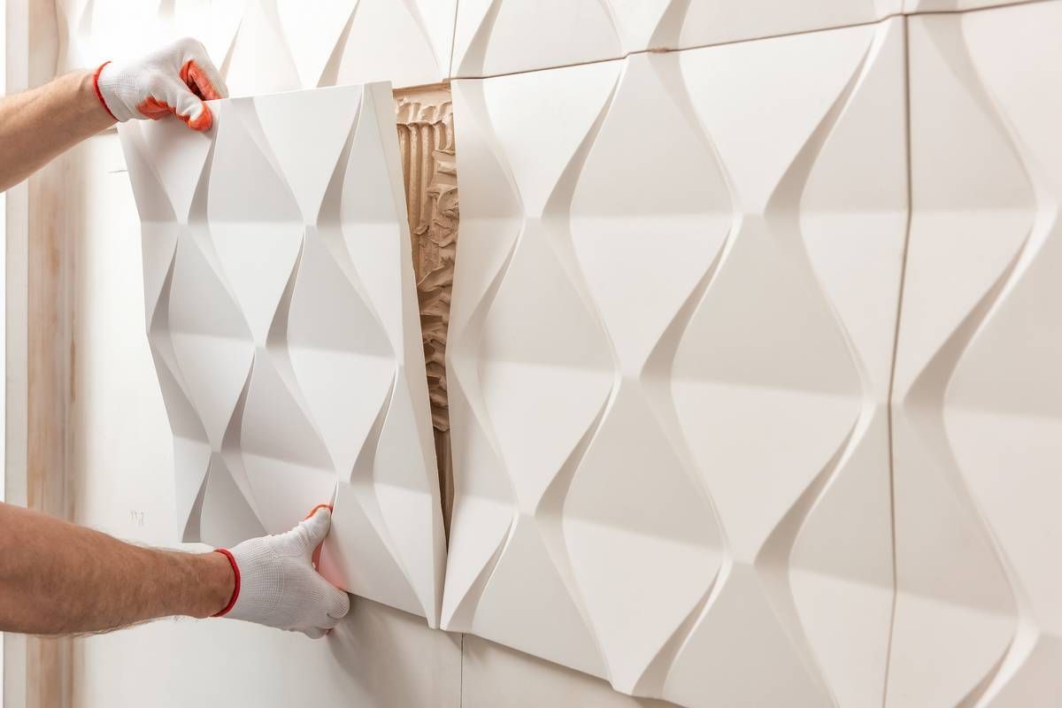 Hands installing white geometric wall panels with exposed adhesive and tools visible