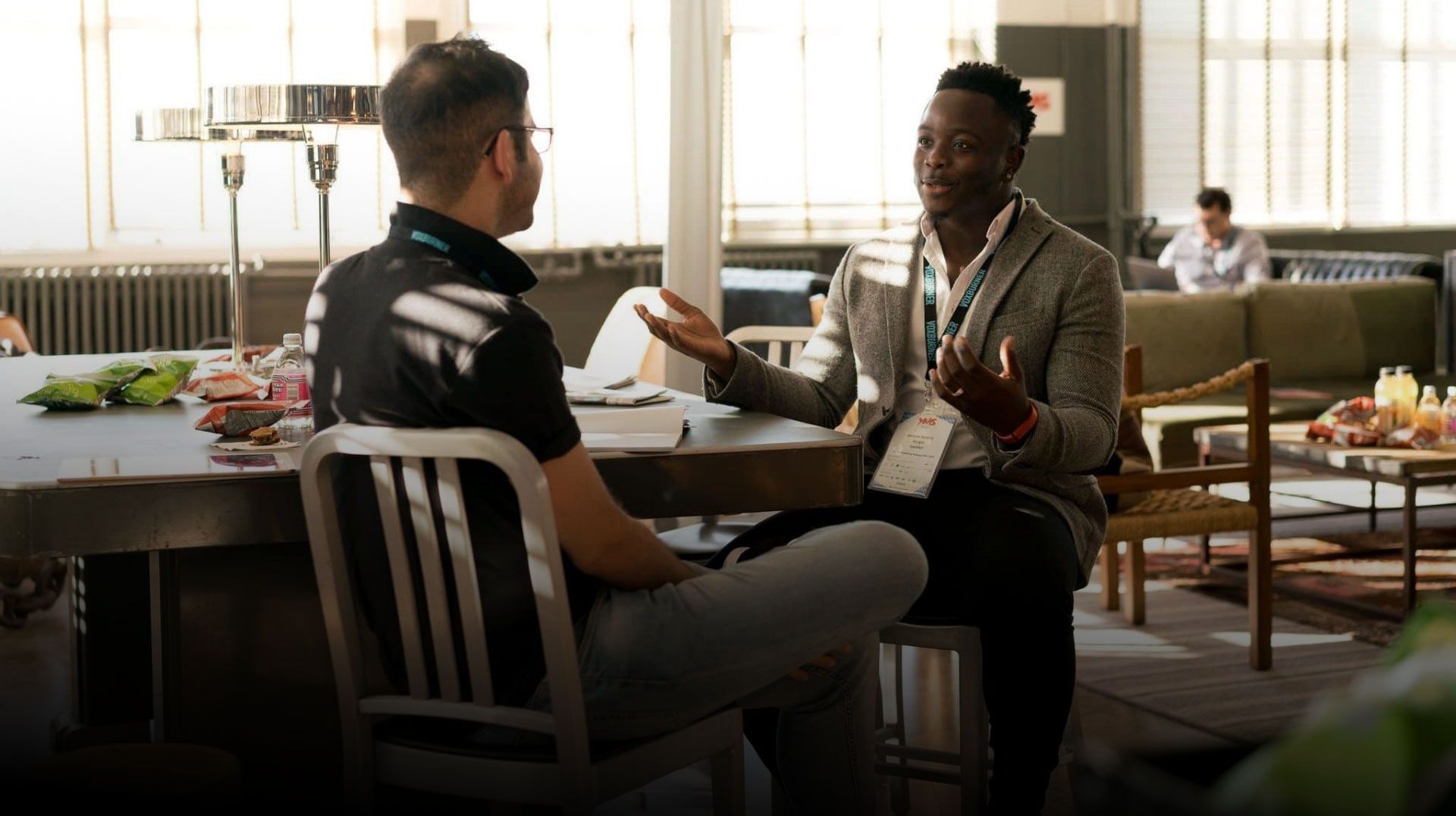 Two men seated at a table, conversing in a bright, modern office setting.