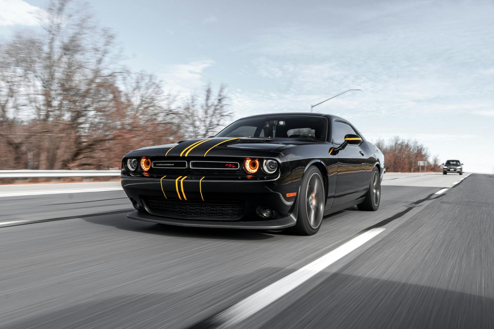 Une Dodge Challenger noire à bandes jaunes roule à vive allure sur l'autoroute.