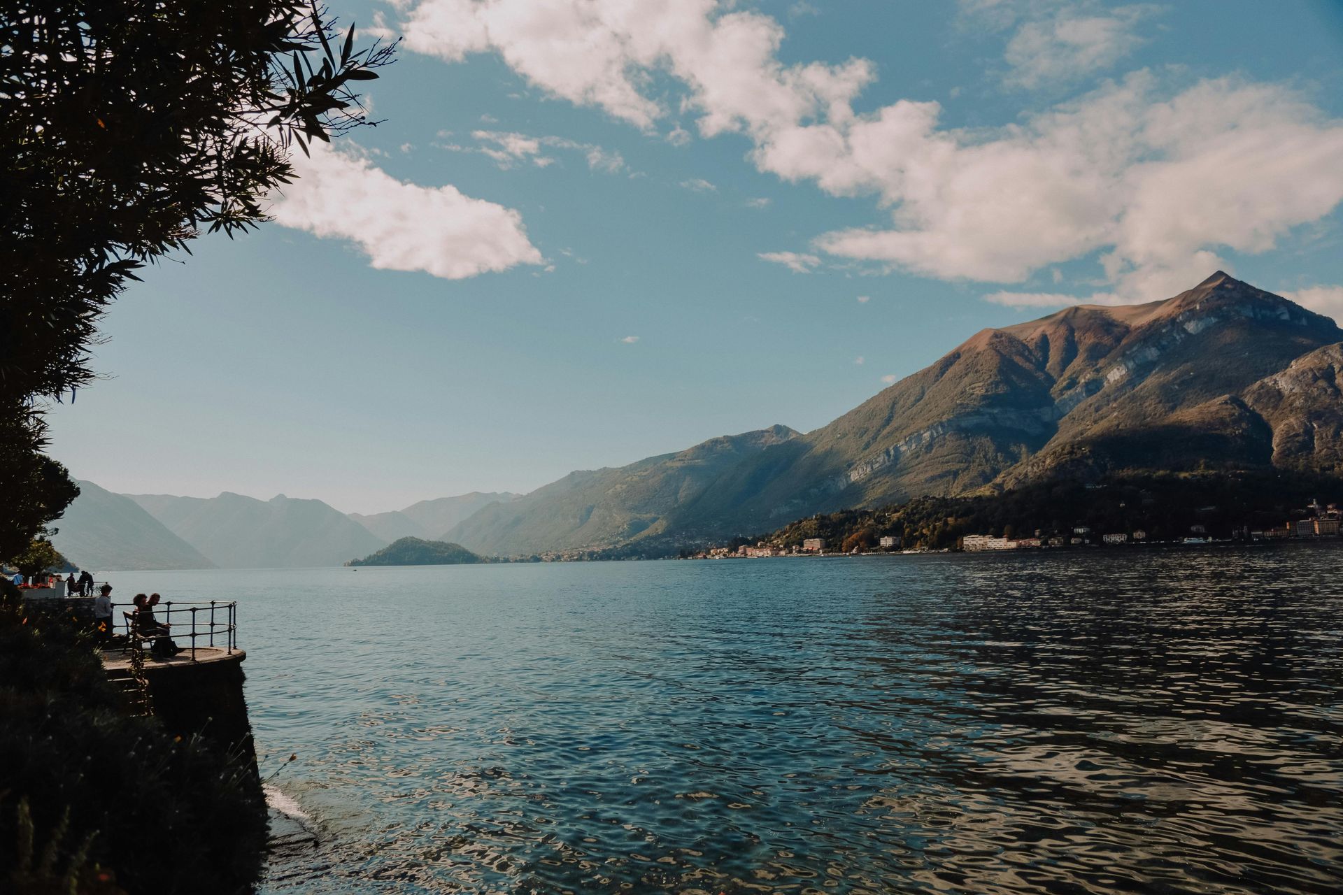 Lac de Côme, Italie. Des montagnes encadrent l'eau sous un ciel bleu parsemé de nuages cotonneux.