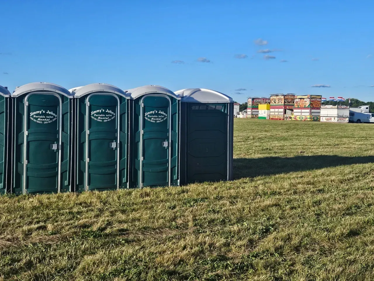 A row of green portable toilets are lined up in a grassy field.