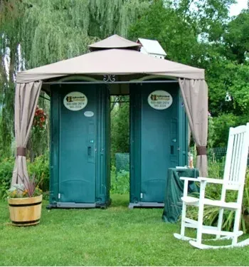 Two portable toilets under an umbrella.