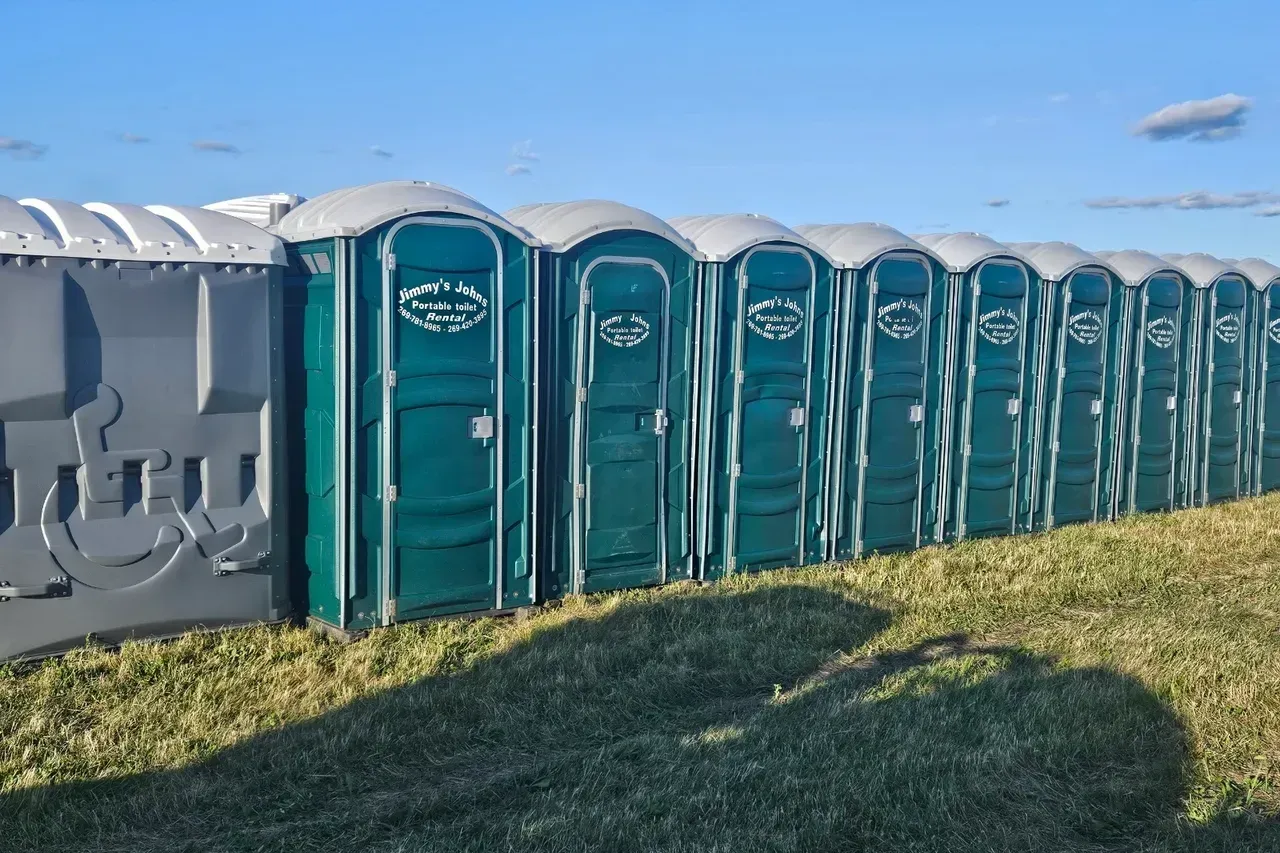 A row of portable toilets are lined up in a grassy field.