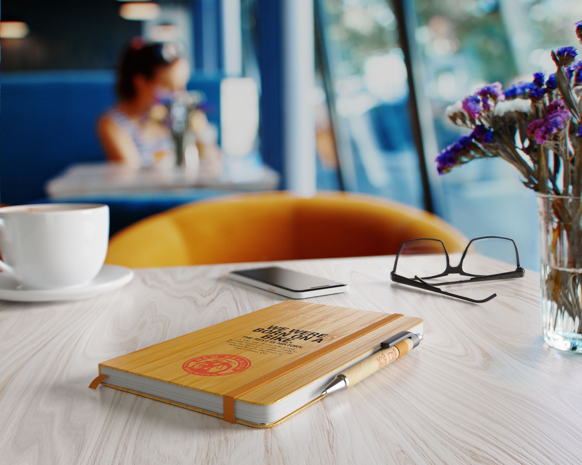 A notebook and pen are on a table next to a vase of flowers
