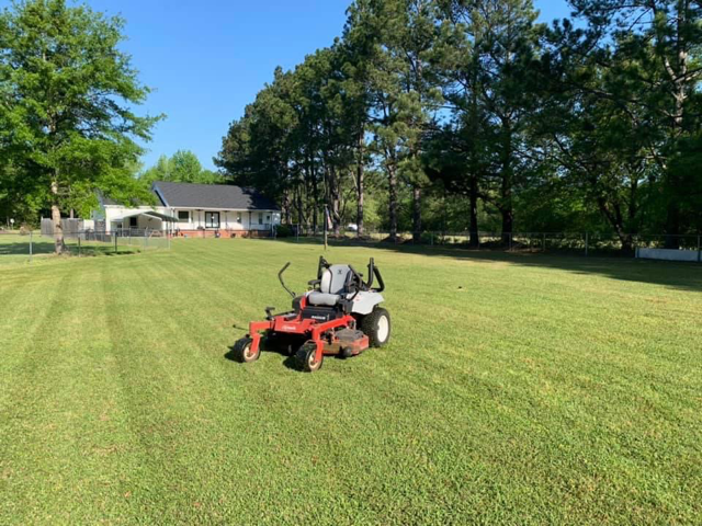 Red riding mower on a green lawn with trees and a house in the background