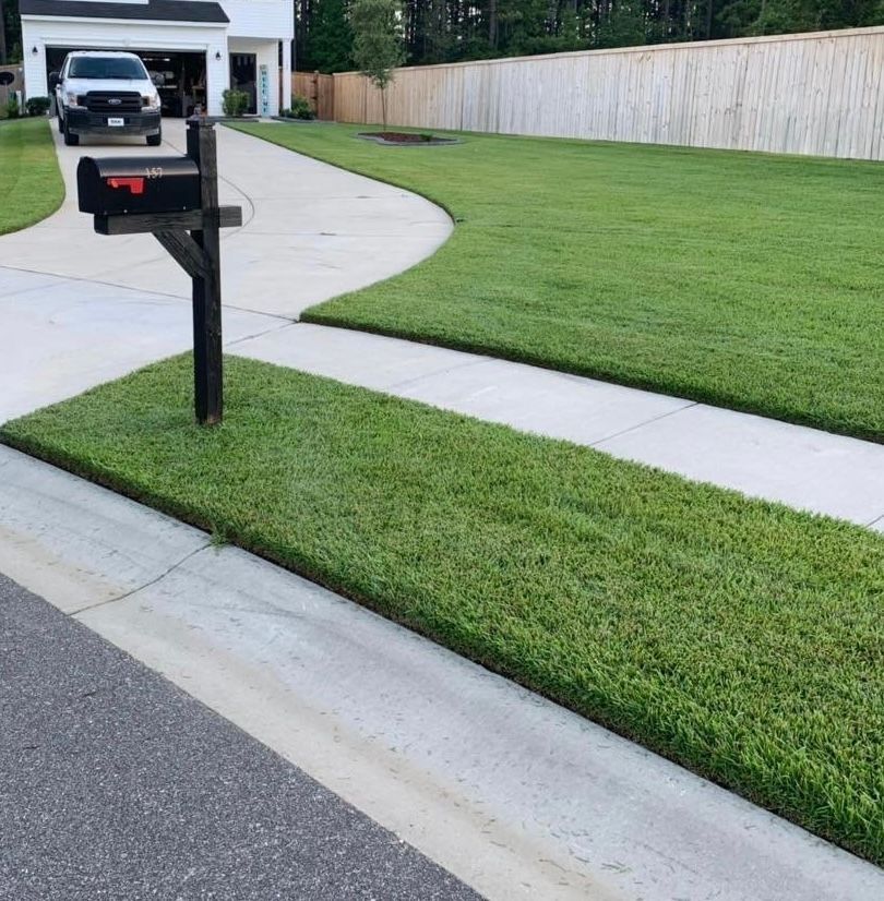 Mailbox beside a curved driveway in front of a house, with neatly trimmed lawn and white fence