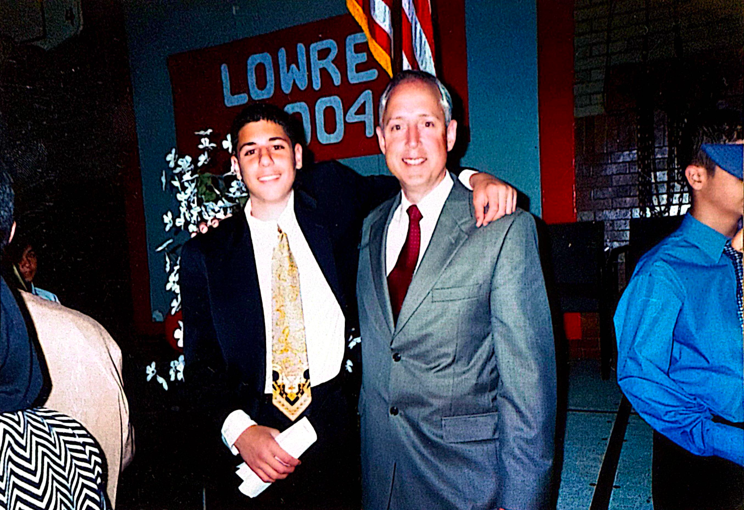 Two men smiling and posing for a photo. One has arm around the other. Lowrey sign in background.