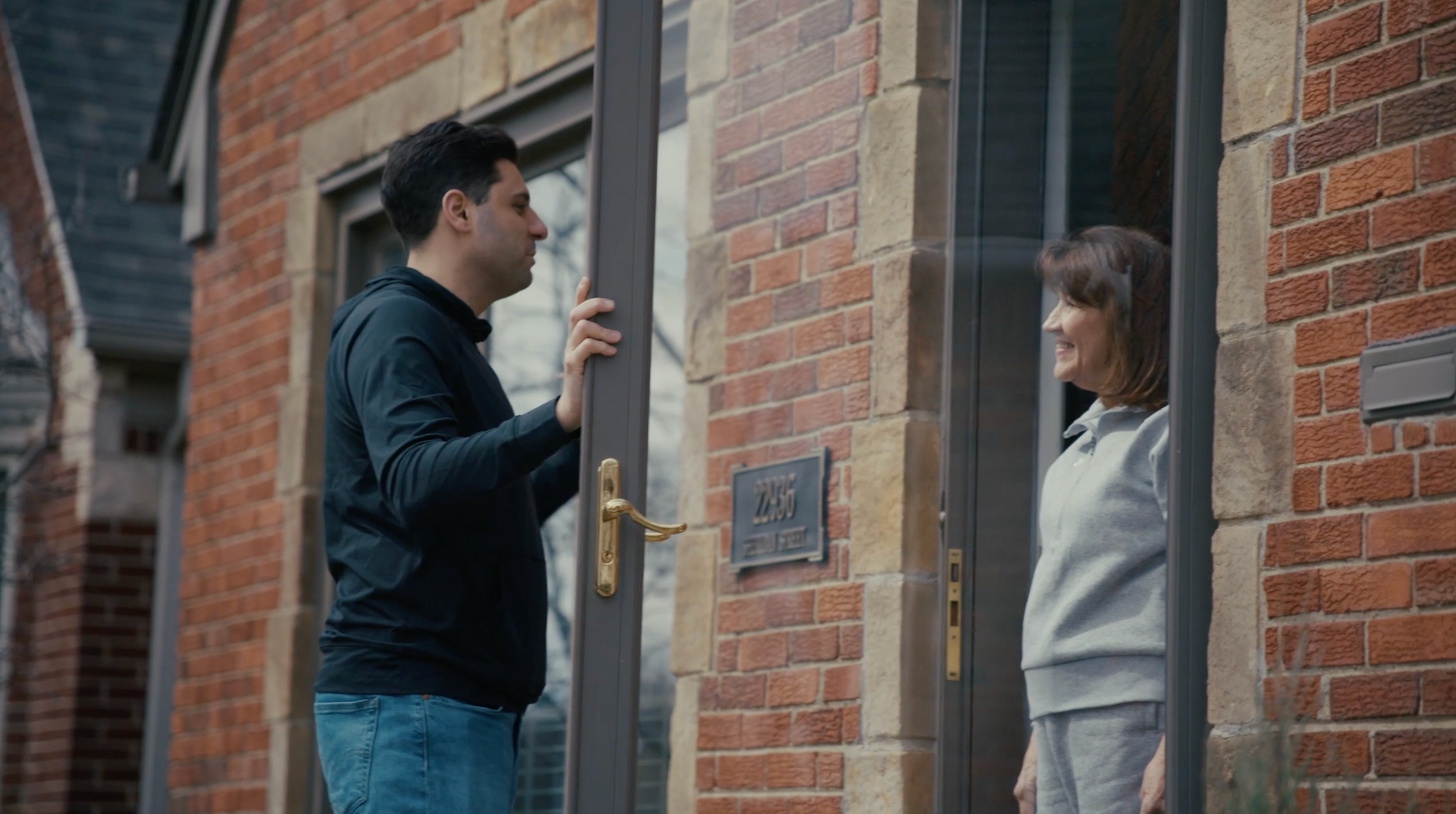 Man holding a door open for a woman outside a brick building.