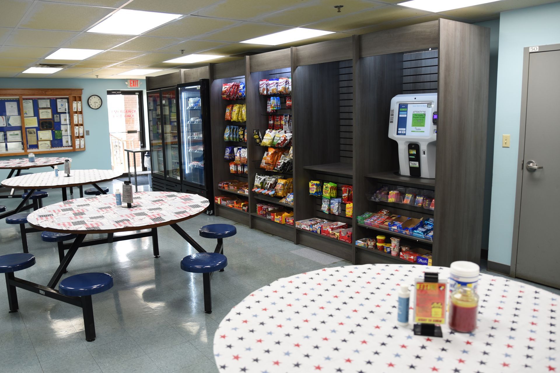 A room with tables and chairs and a vending machine.