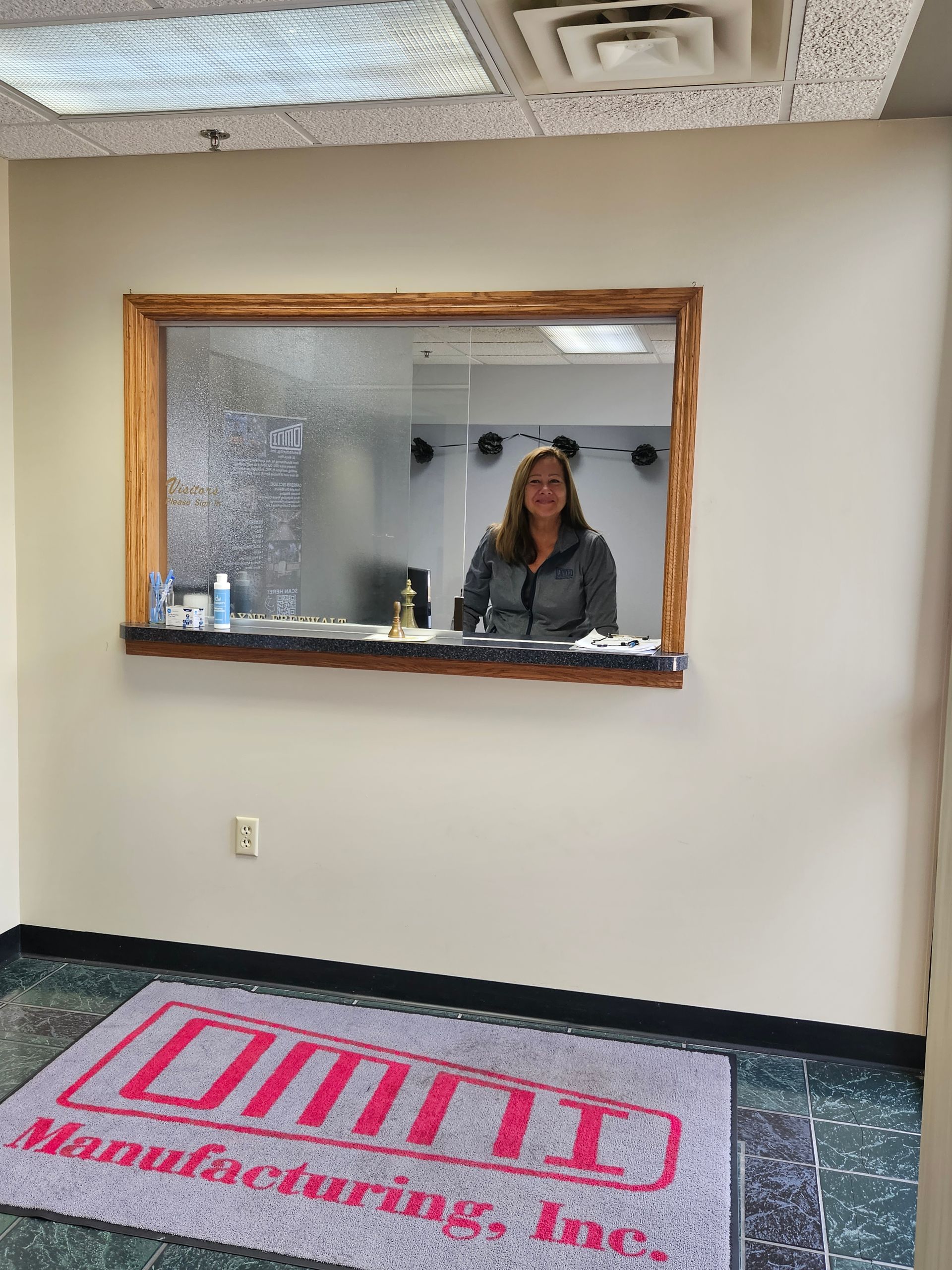 A woman is standing in front of a window in a room with a rug that says manufacturing inc.