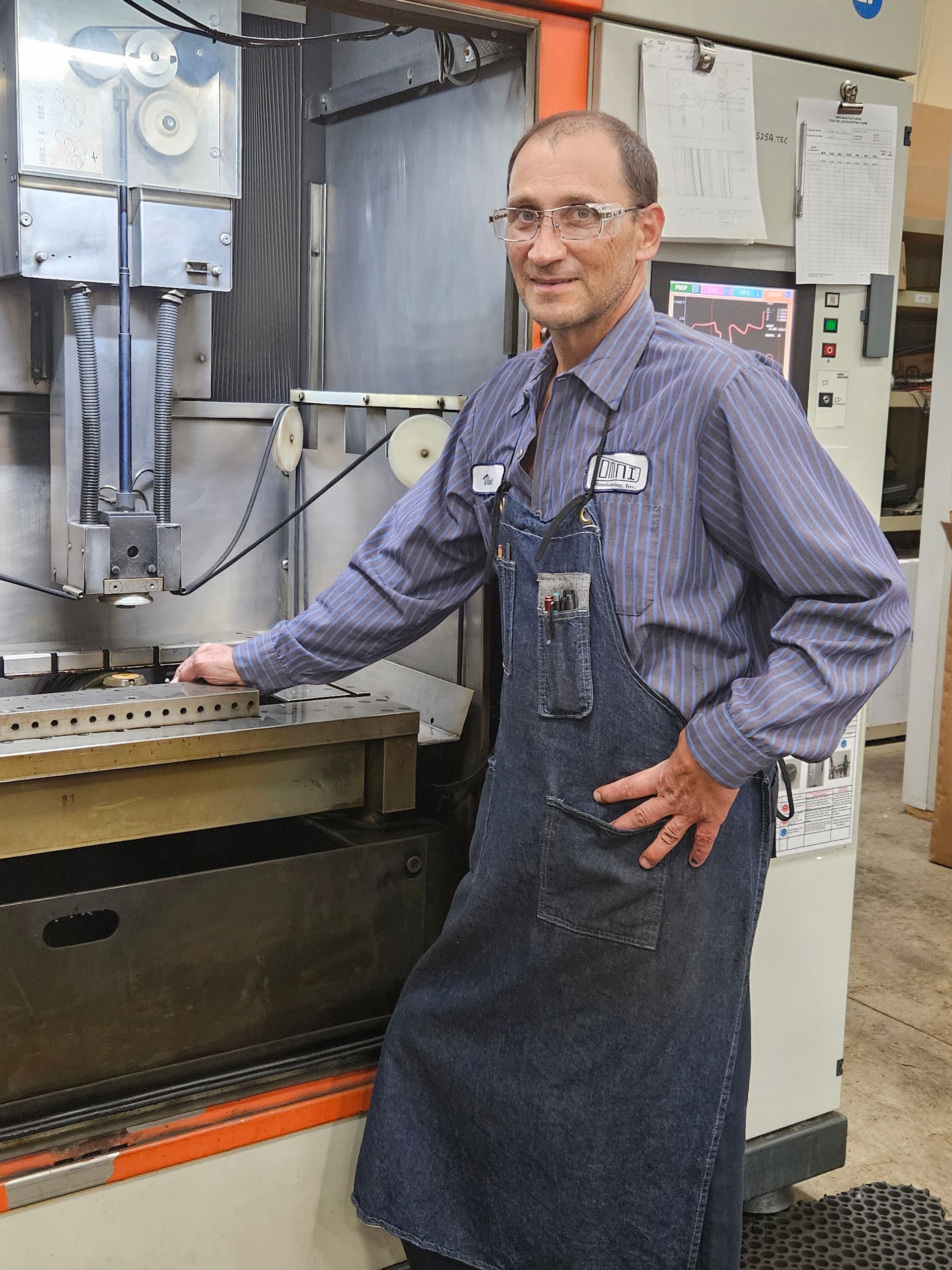 A man in an apron is standing in front of a machine.