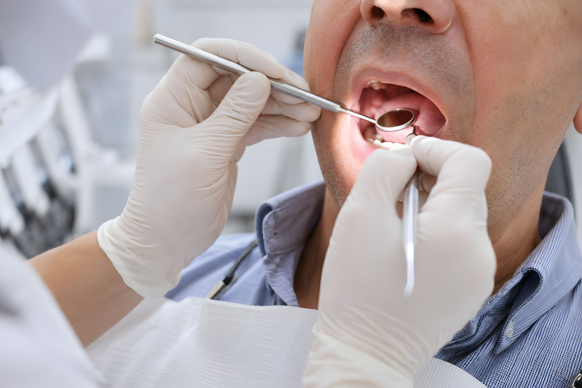 Dentist examining a patient’s open mouth with dental tools and gloved hands