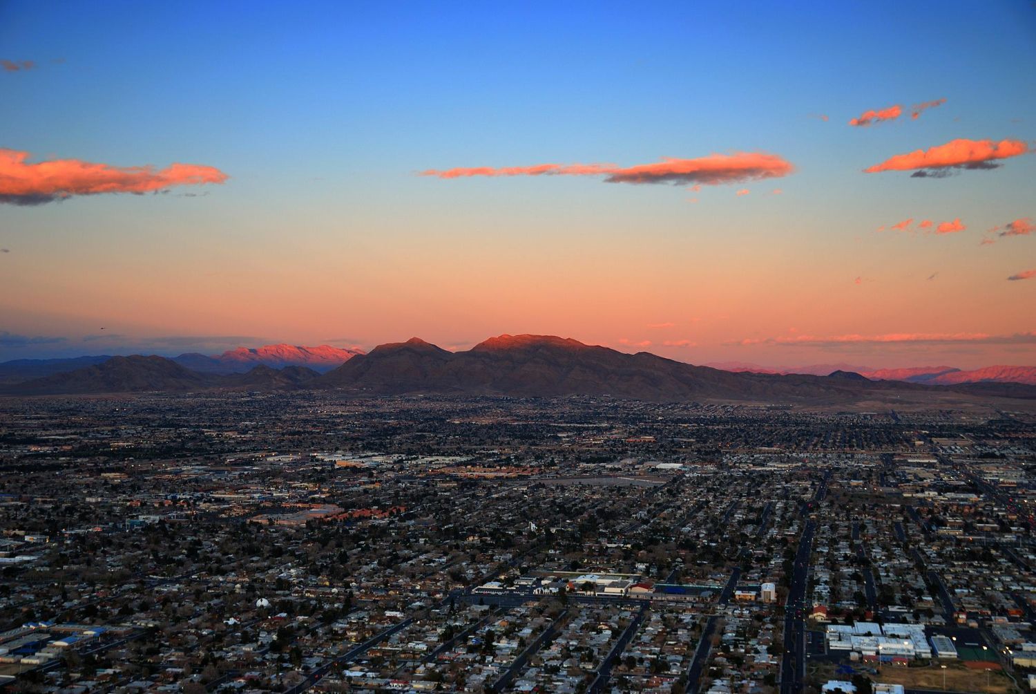 City skyline with mountains at dusk; orange and blue sky.