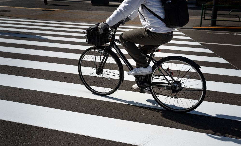Cyclist on black bicycle crossing a white crosswalk. Sunny day.