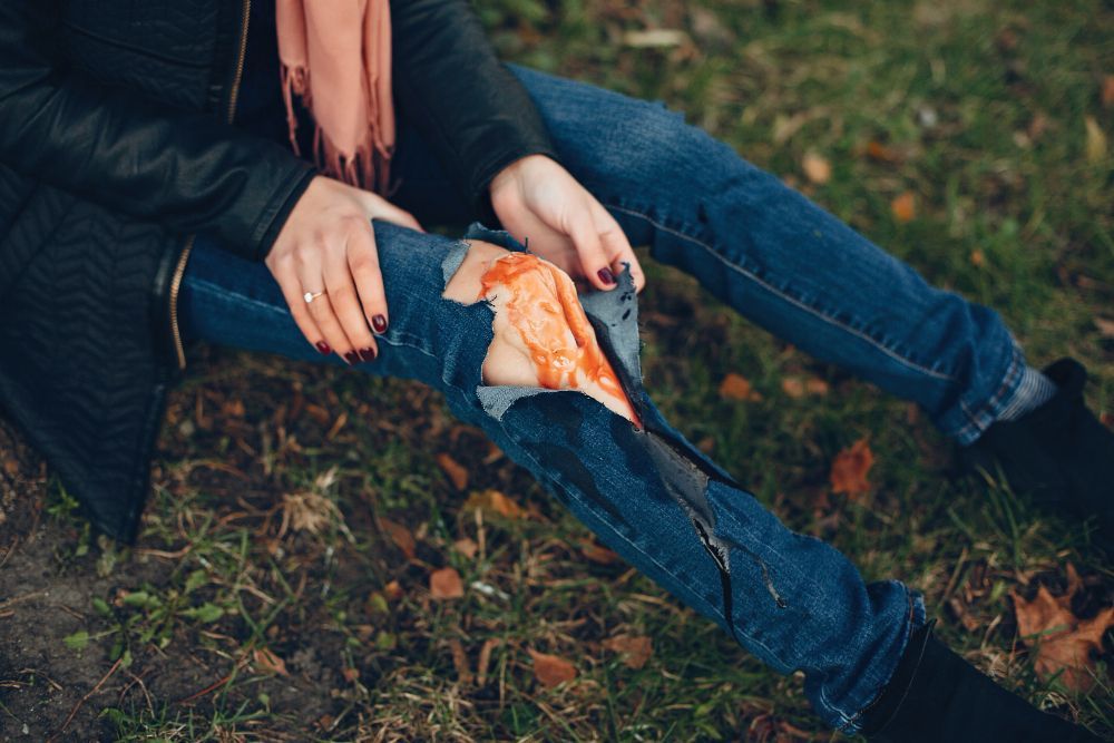 Person with a bloody knee wound, sitting on grass, jean pants ripped.