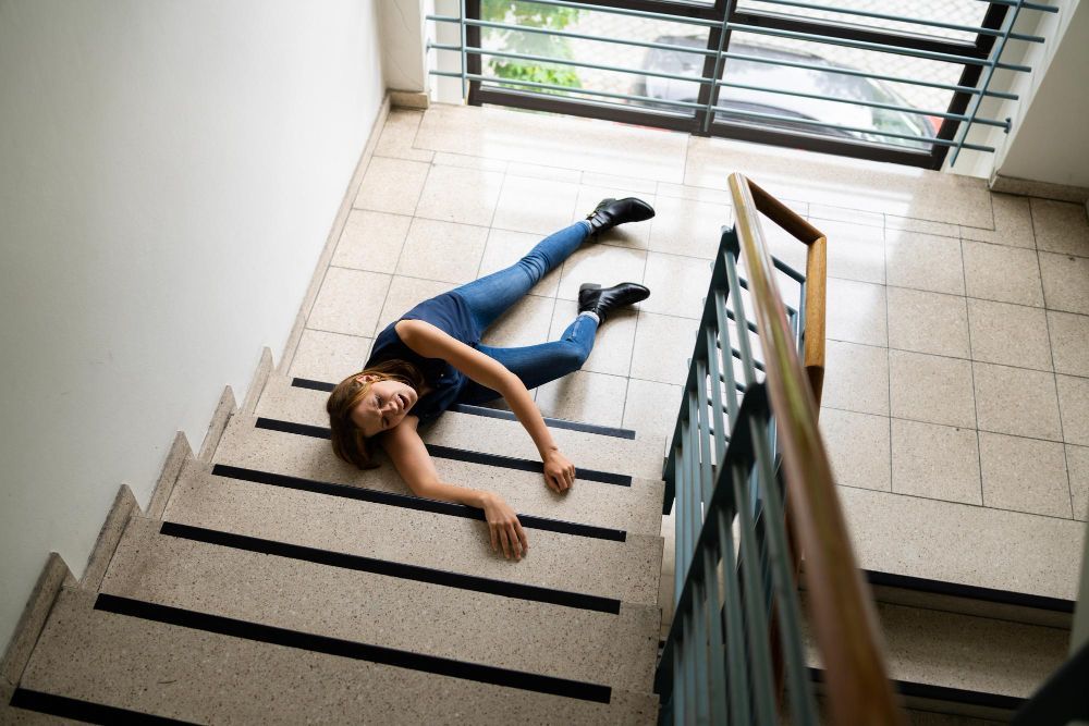 Person lying at the bottom of stairs, likely after a fall. Stairwell setting, tiled floor.