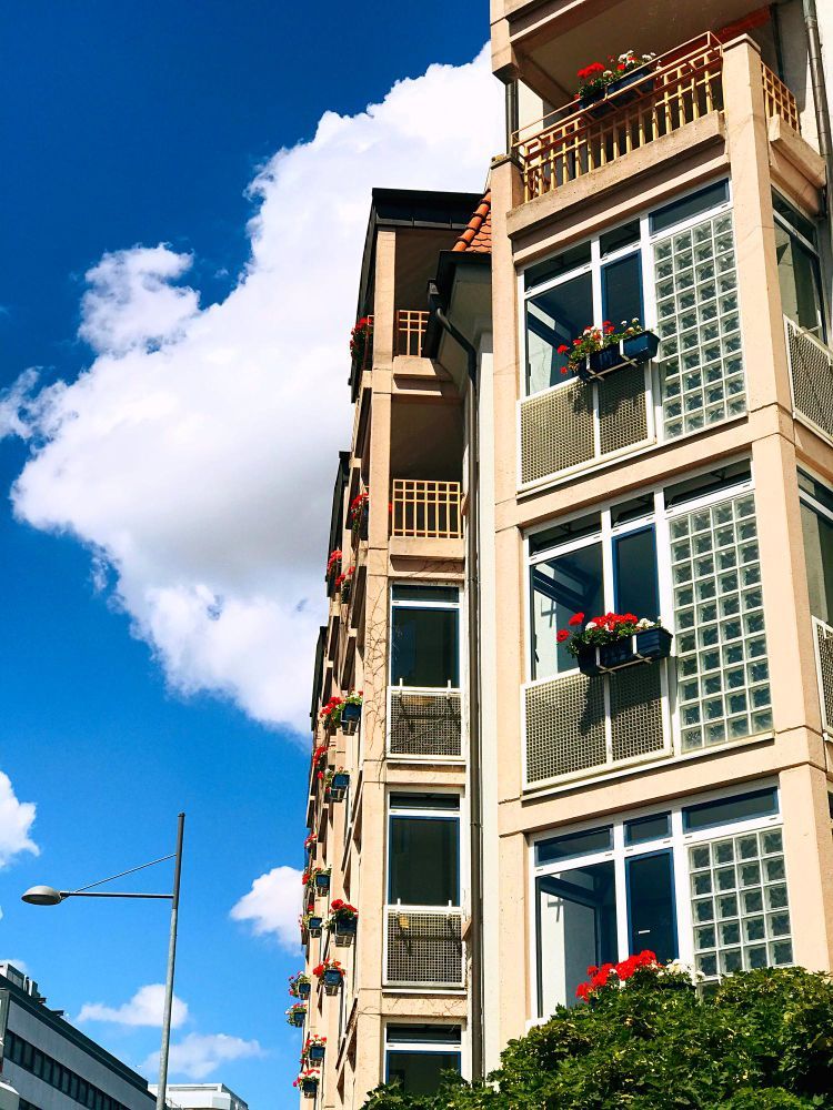 Building with balconies, window boxes with red flowers, against a blue sky with fluffy white clouds.