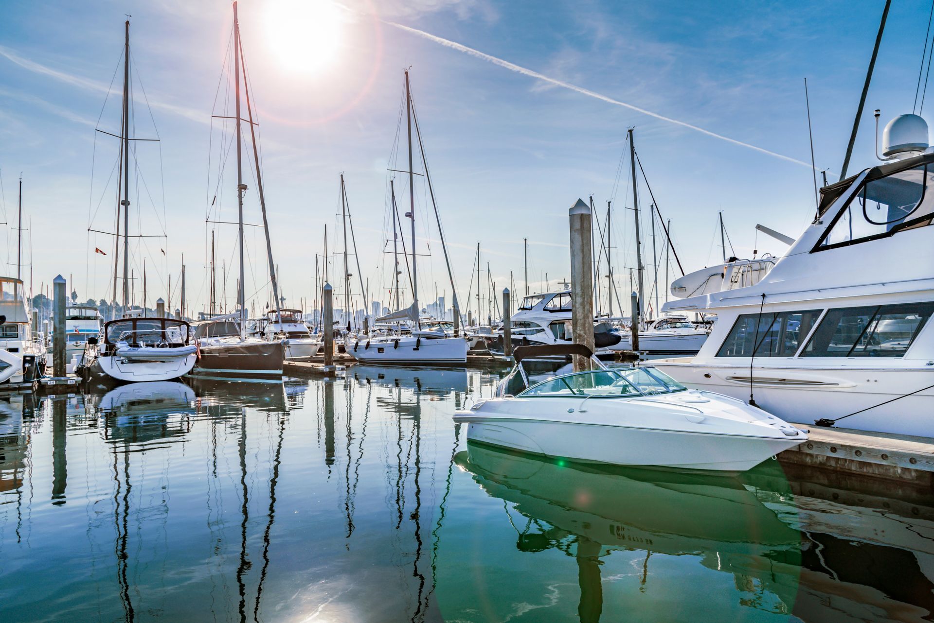 Boats docked in a sunny harbor, masts and reflections in the water.