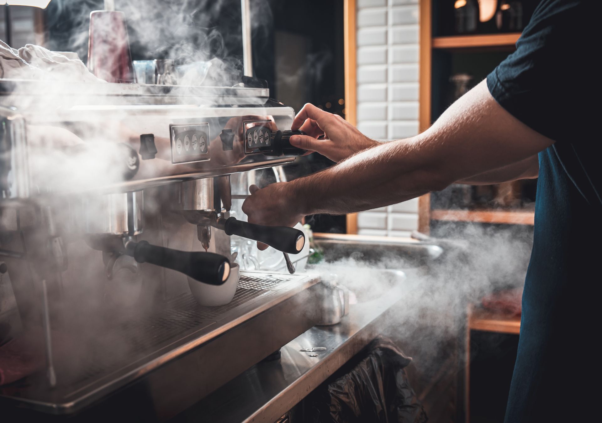 Barista operating espresso machine, steam billowing, indoors.