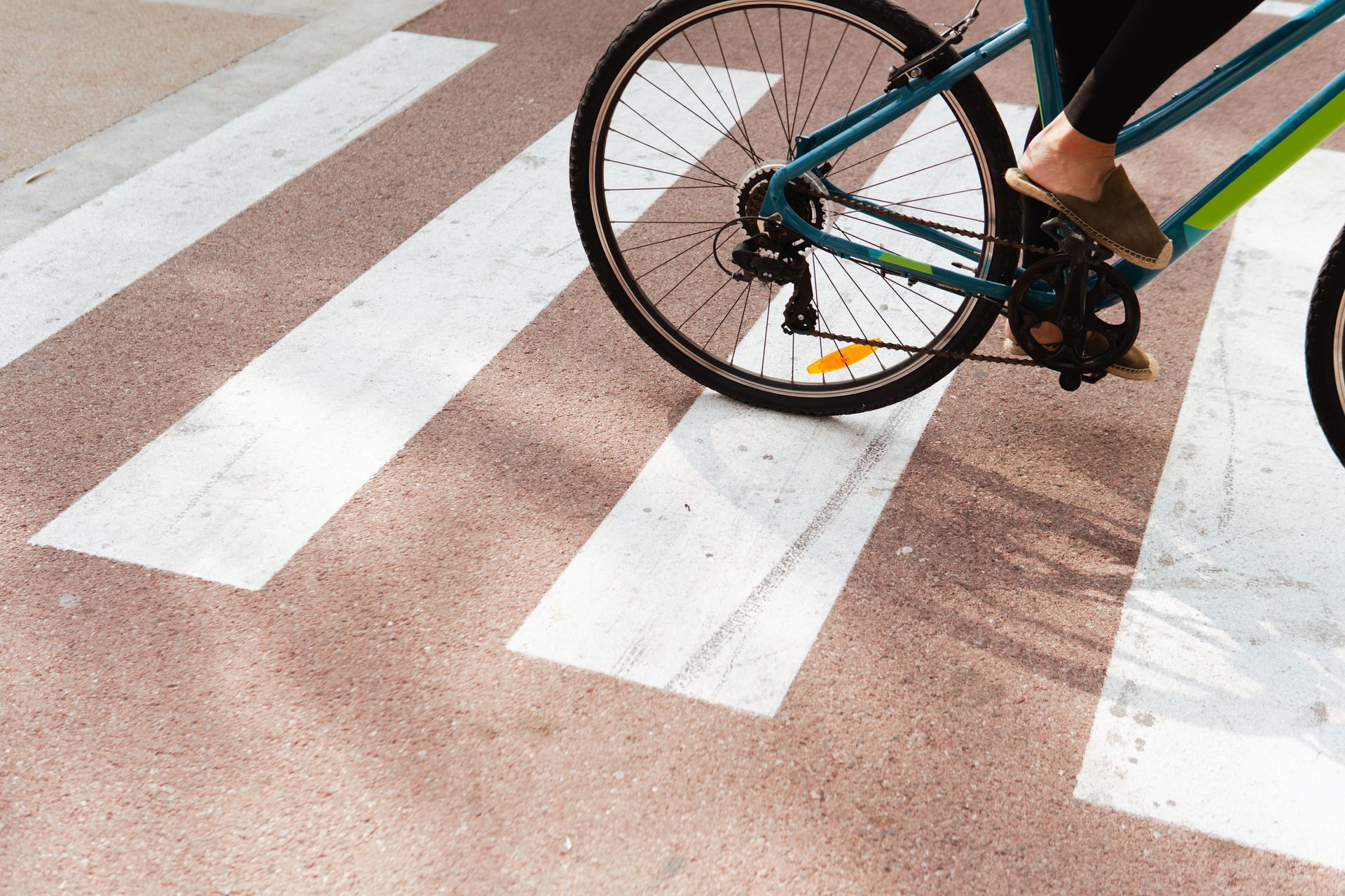 Bicyclist riding over a crosswalk. Bicycle is blue and green, person's foot visible in sandals.