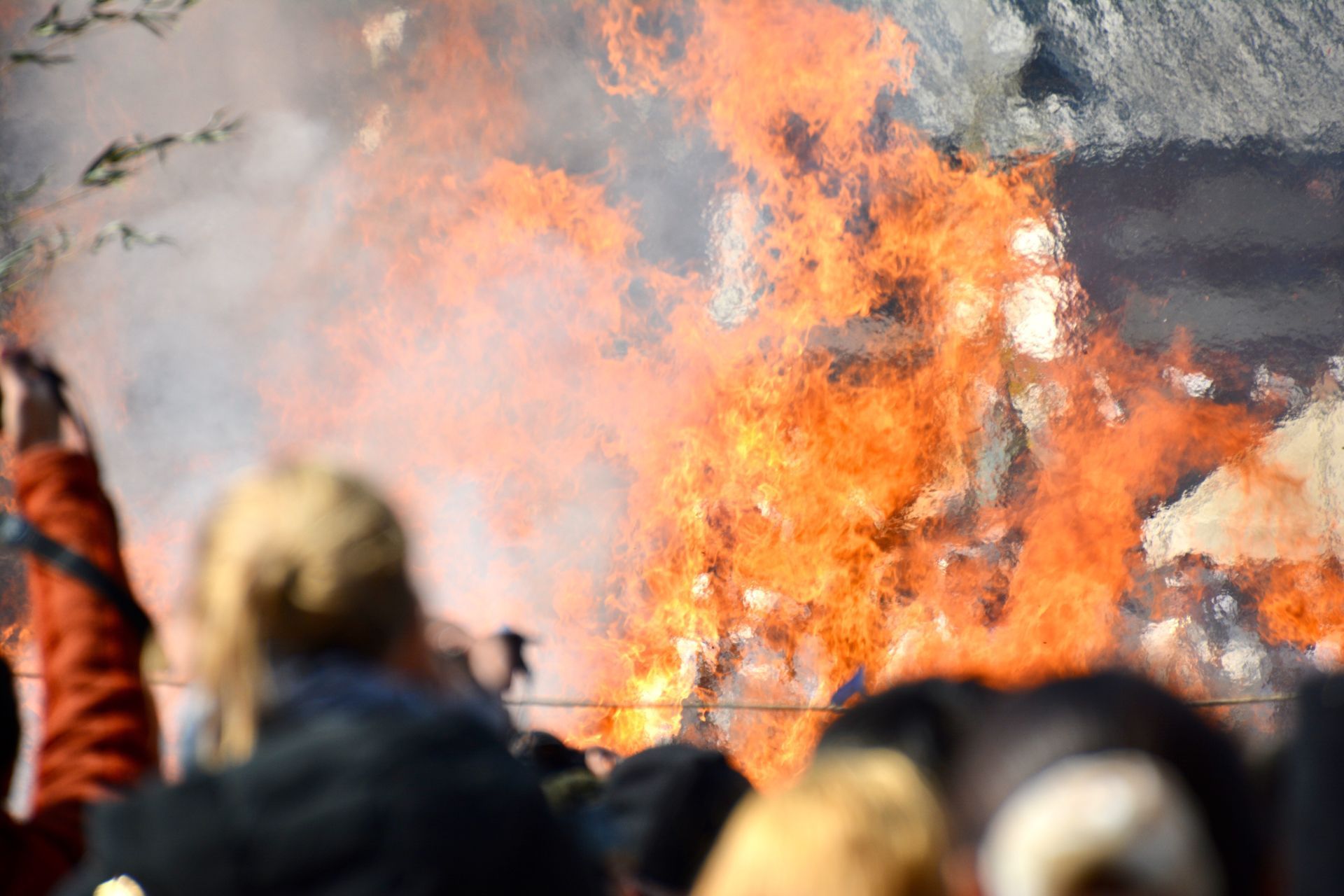 Flames erupt from a building, with blurred people watching in the foreground.