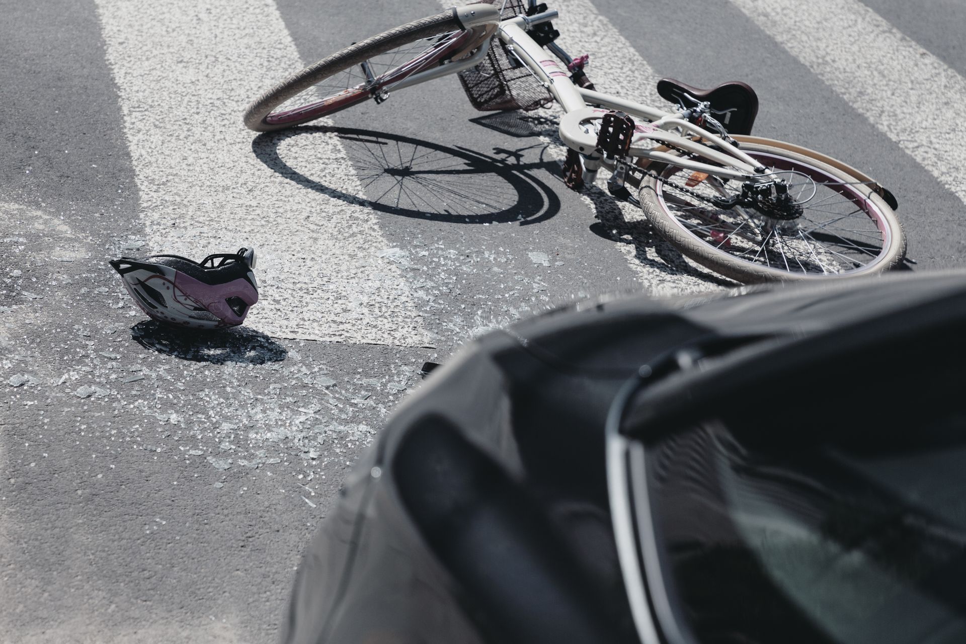 Bicycle and helmet on a crosswalk after a collision with a black car.