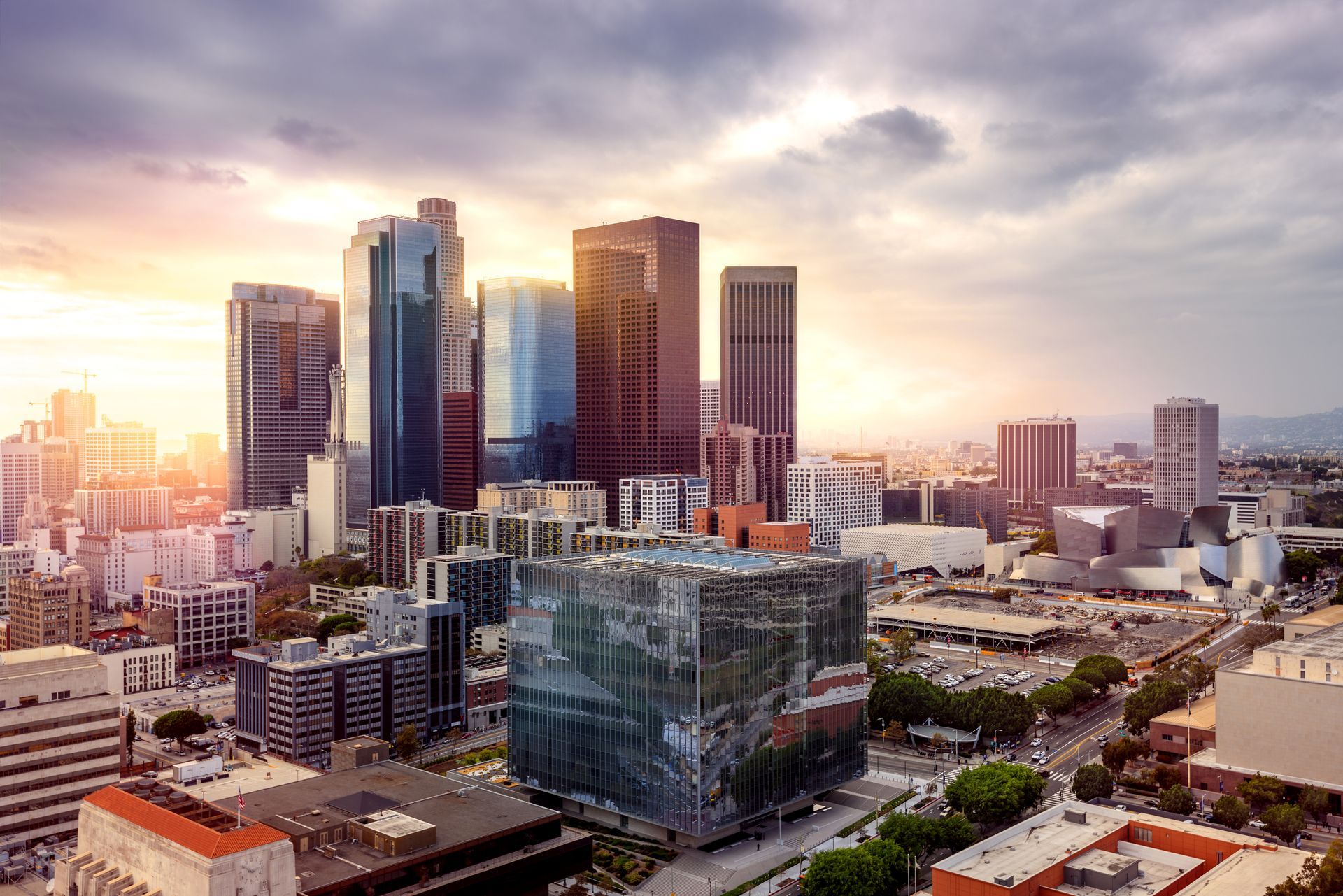Downtown Los Angeles skyline at sunset, with tall skyscrapers and a cloudy sky.