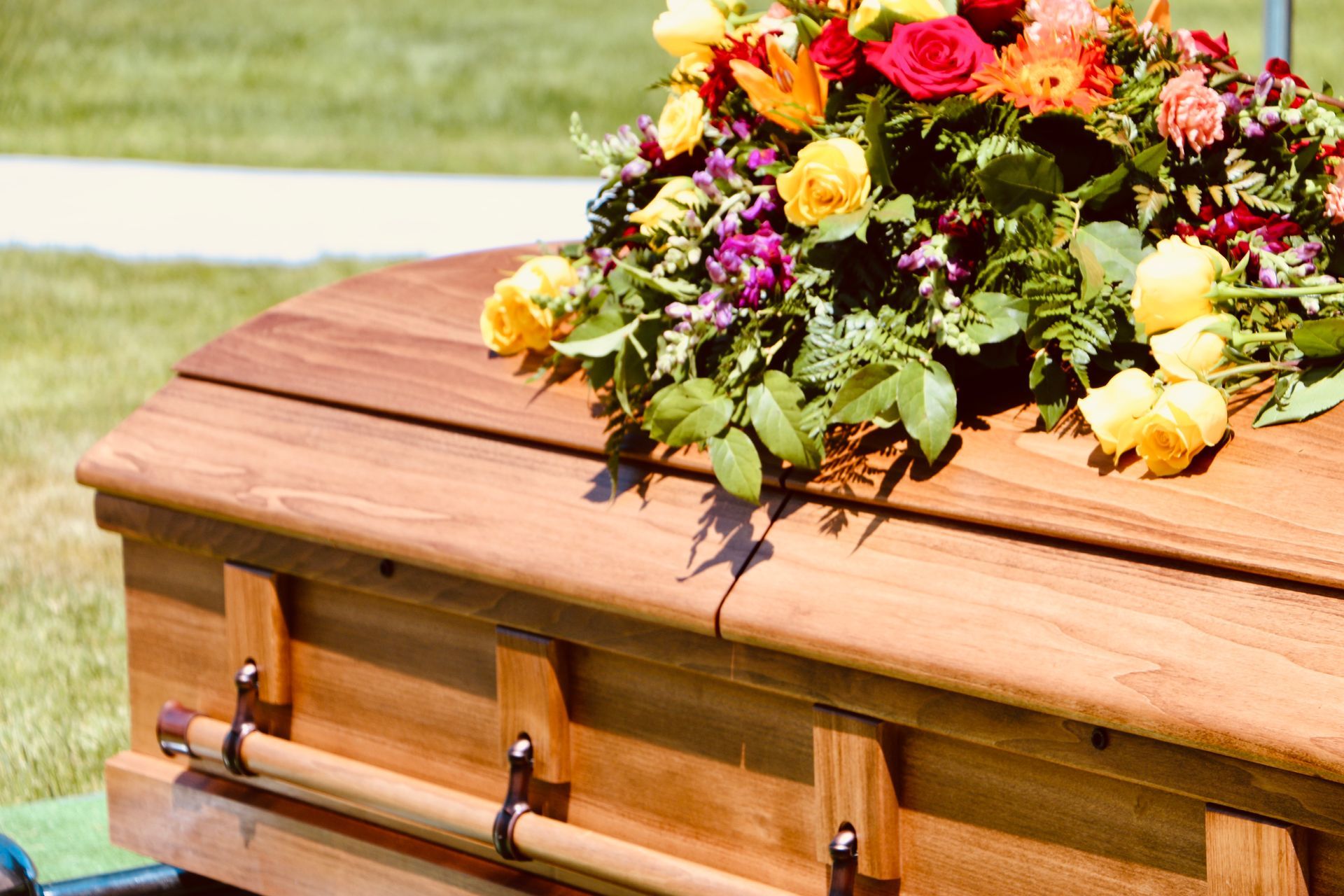 Wooden casket with a floral arrangement on top, outdoors on grass.