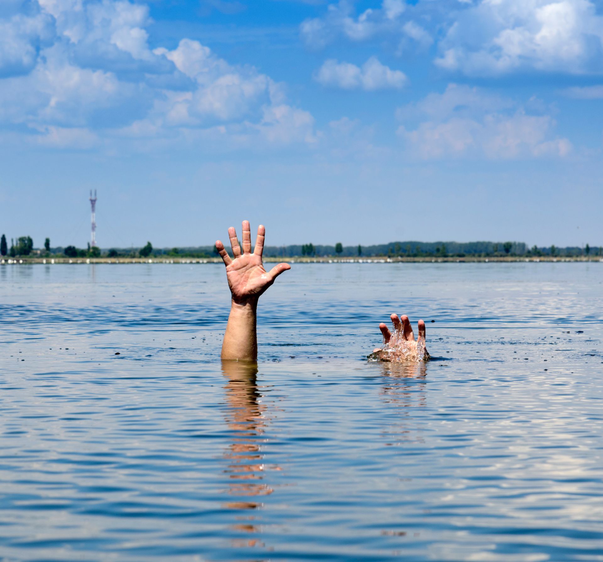 Two hands reaching up from water, possibly drowning, under a blue sky.