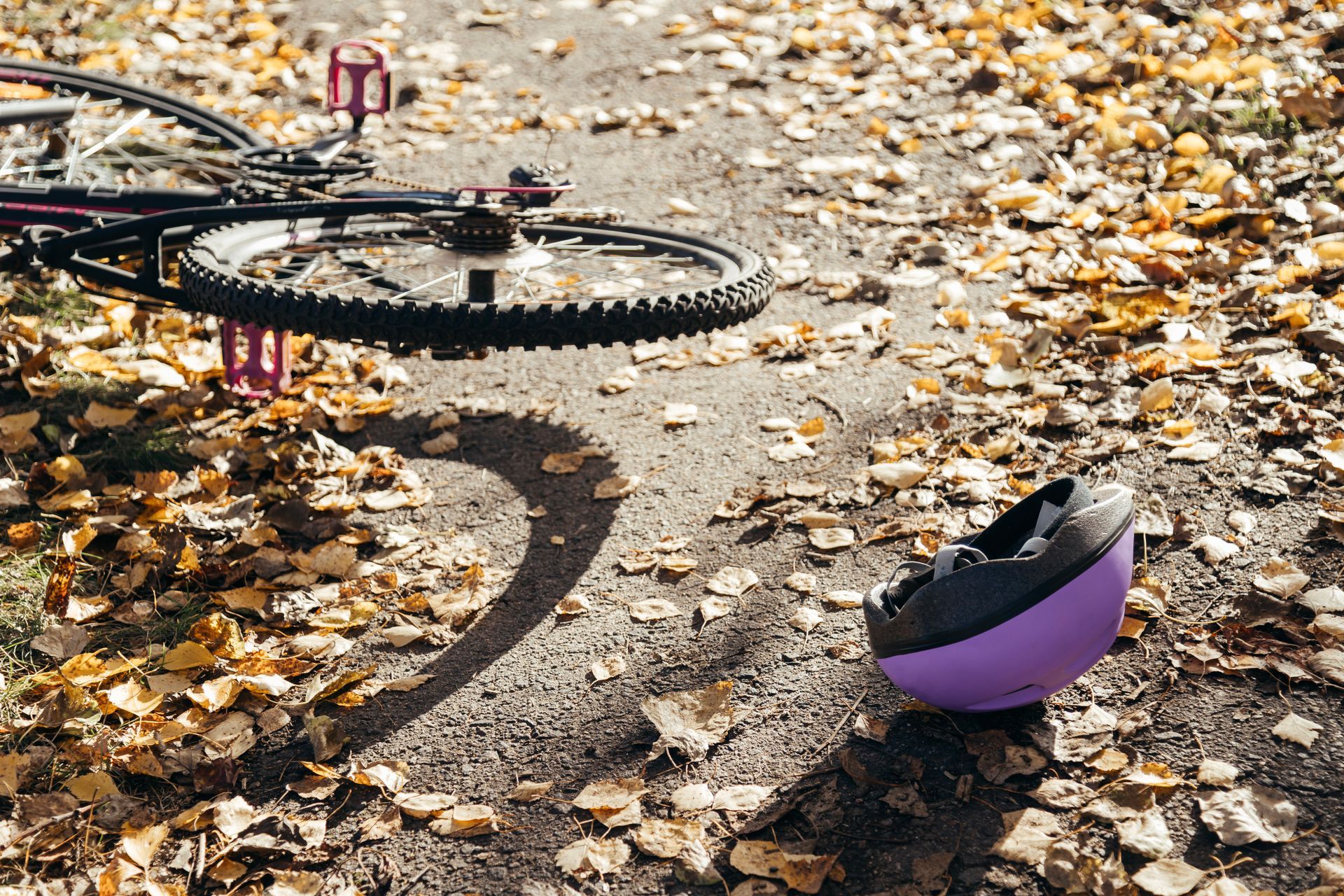 Bicycle lying on a path covered in leaves with a purple helmet nearby.