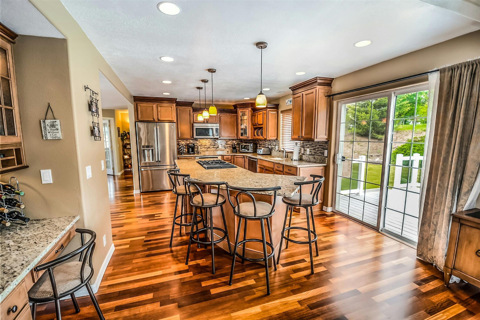 A kitchen with a large island and stools and a sliding glass door.