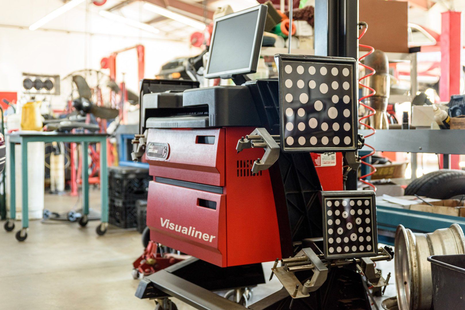 Red and black wheel alignment machine in a garage setting with a computer monitor.