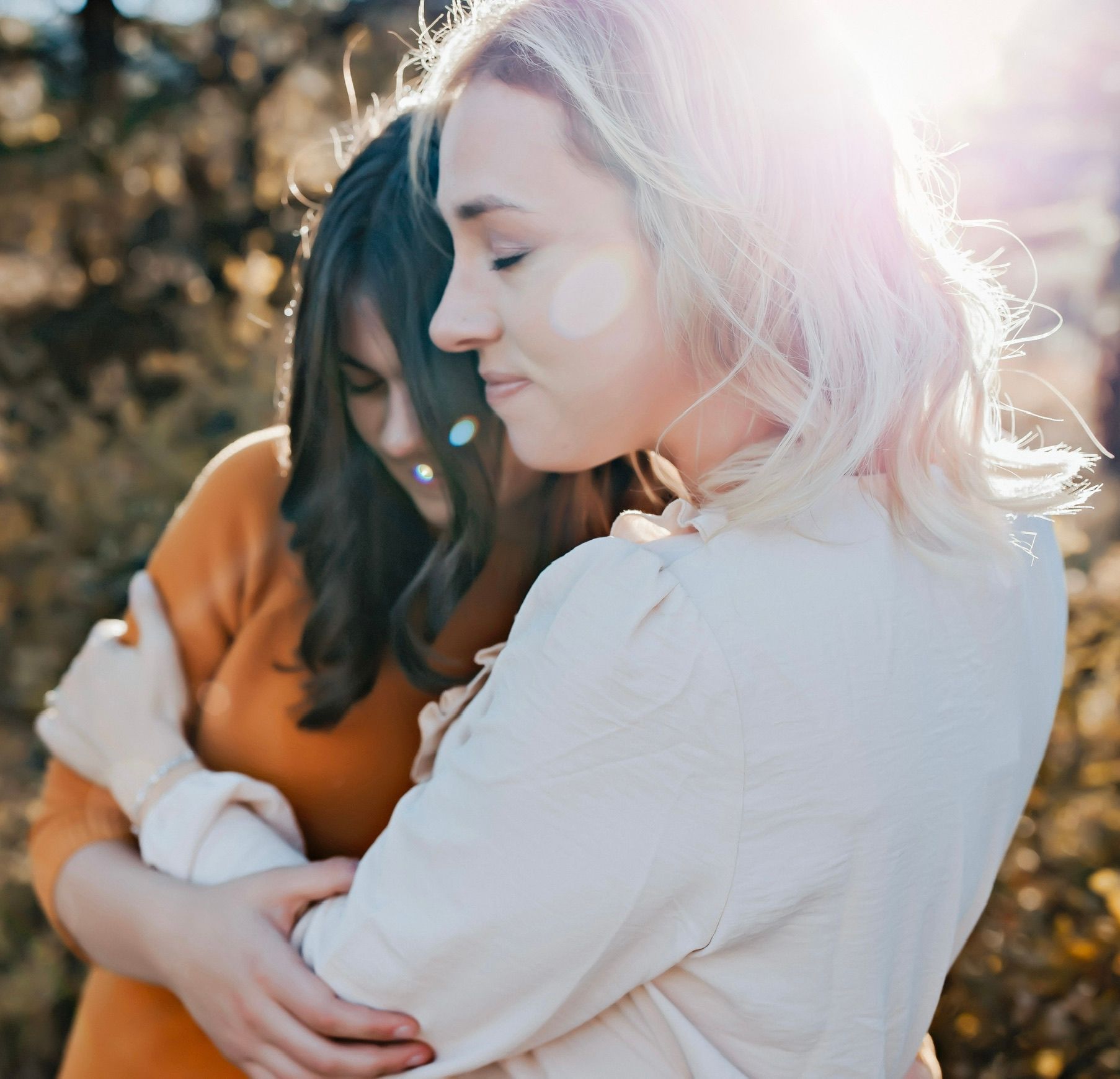 Two women hugging each other with the sun shining through the trees