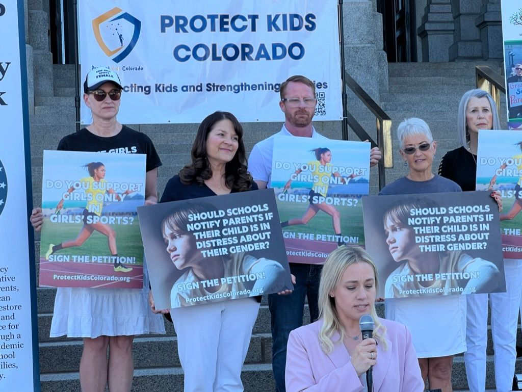 A group of people holding signs in front of a sign that says protect kids colorado