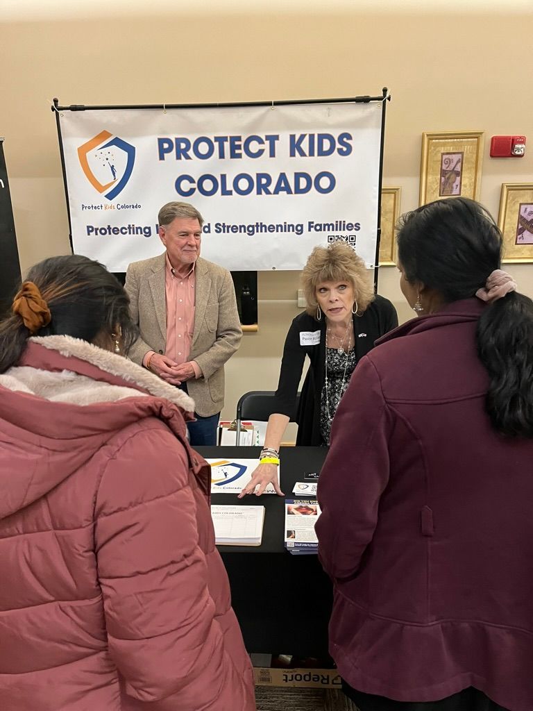 A group of people are standing around a table in front of a sign that says protect kids colorado.