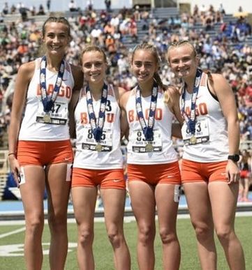 Four female athletes posing for a picture with medals on their shirts