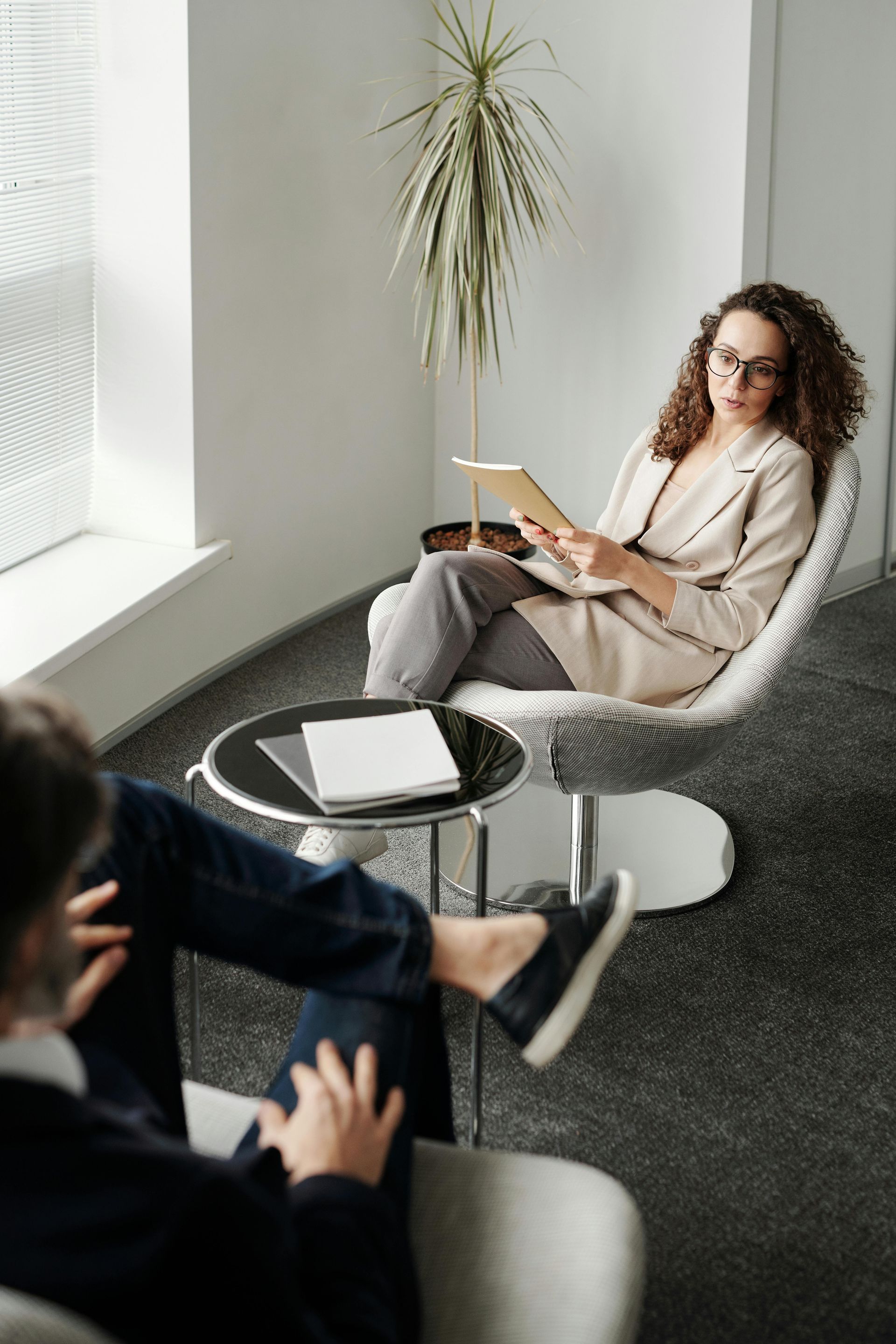 A woman is sitting in a chair reading a book to a man.