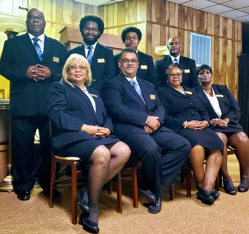 Formal group portrait of six people in suits seated and standing in a wood-paneled room