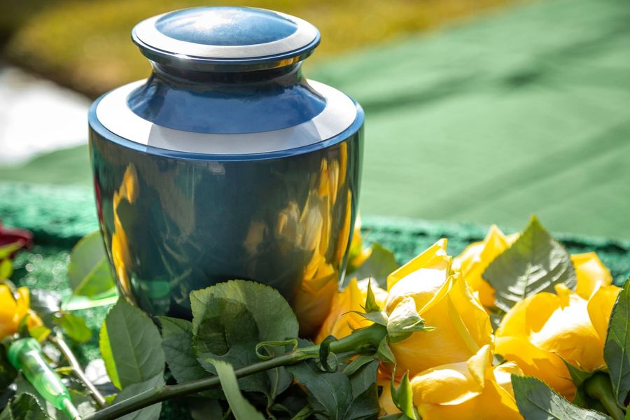 Blue memorial urn surrounded by yellow flowers and green leaves outdoors