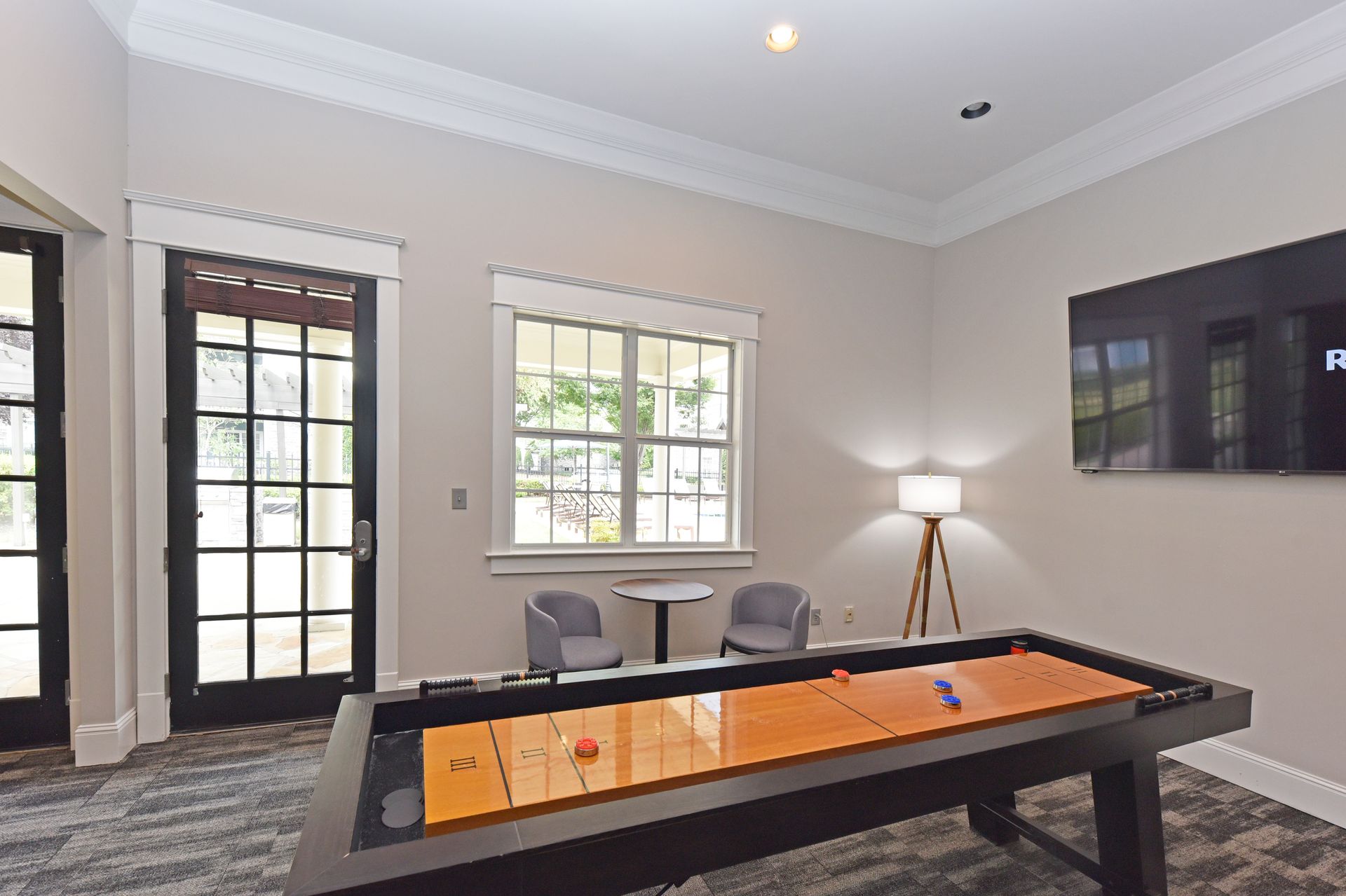 Shuffleboard table in a room with a window, chairs, and a television.