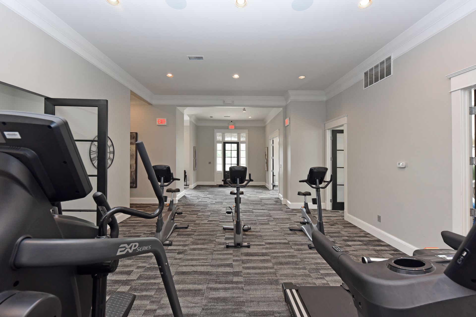 Gym interior with exercise equipment, neutral colors, and a hallway in the background.