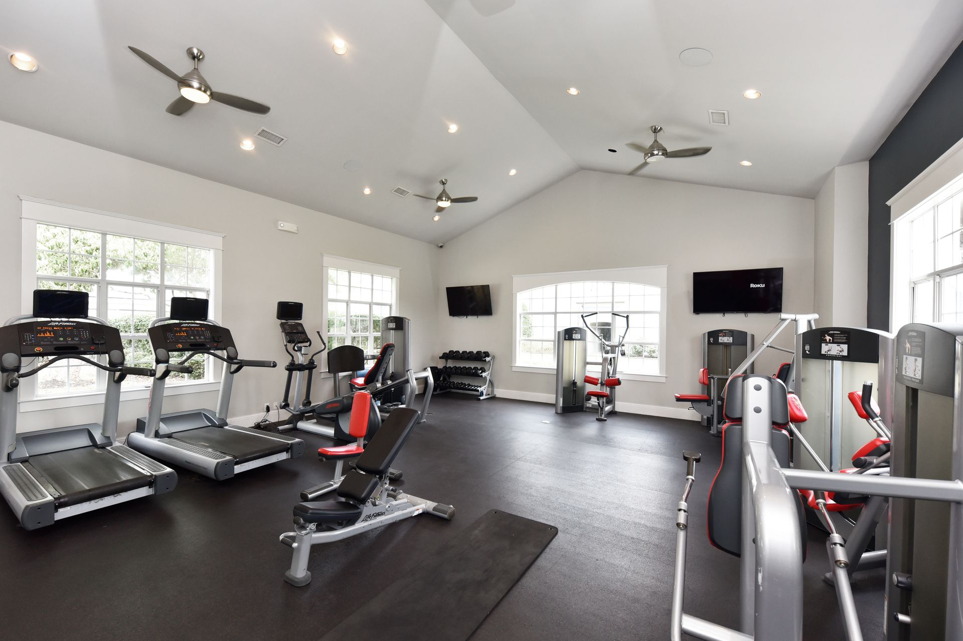 Gym interior with treadmills, weight machines, and free weights; televisions mounted on walls.