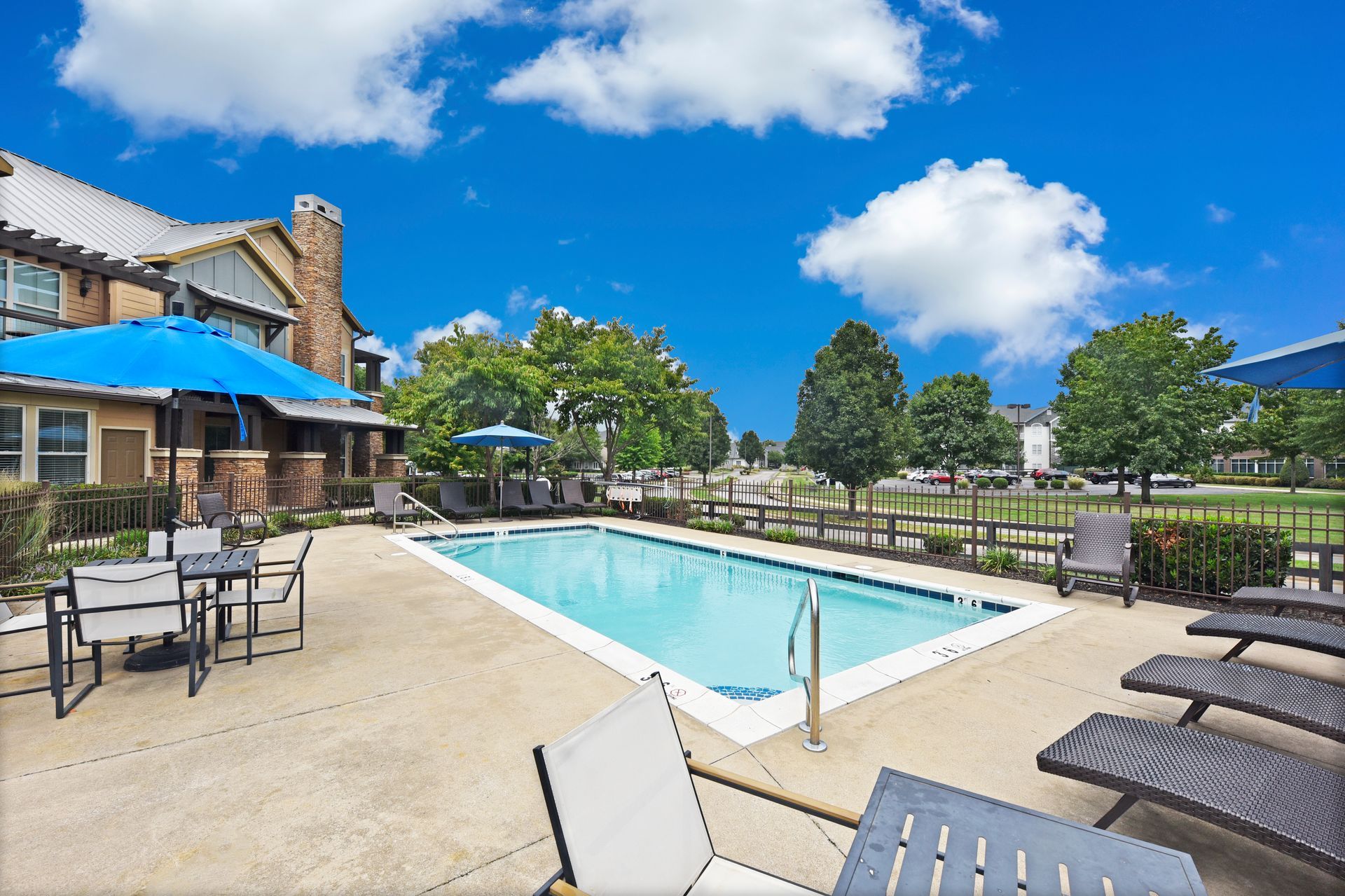 Pool with lounge chairs and umbrellas, blue sky, building in the background.
