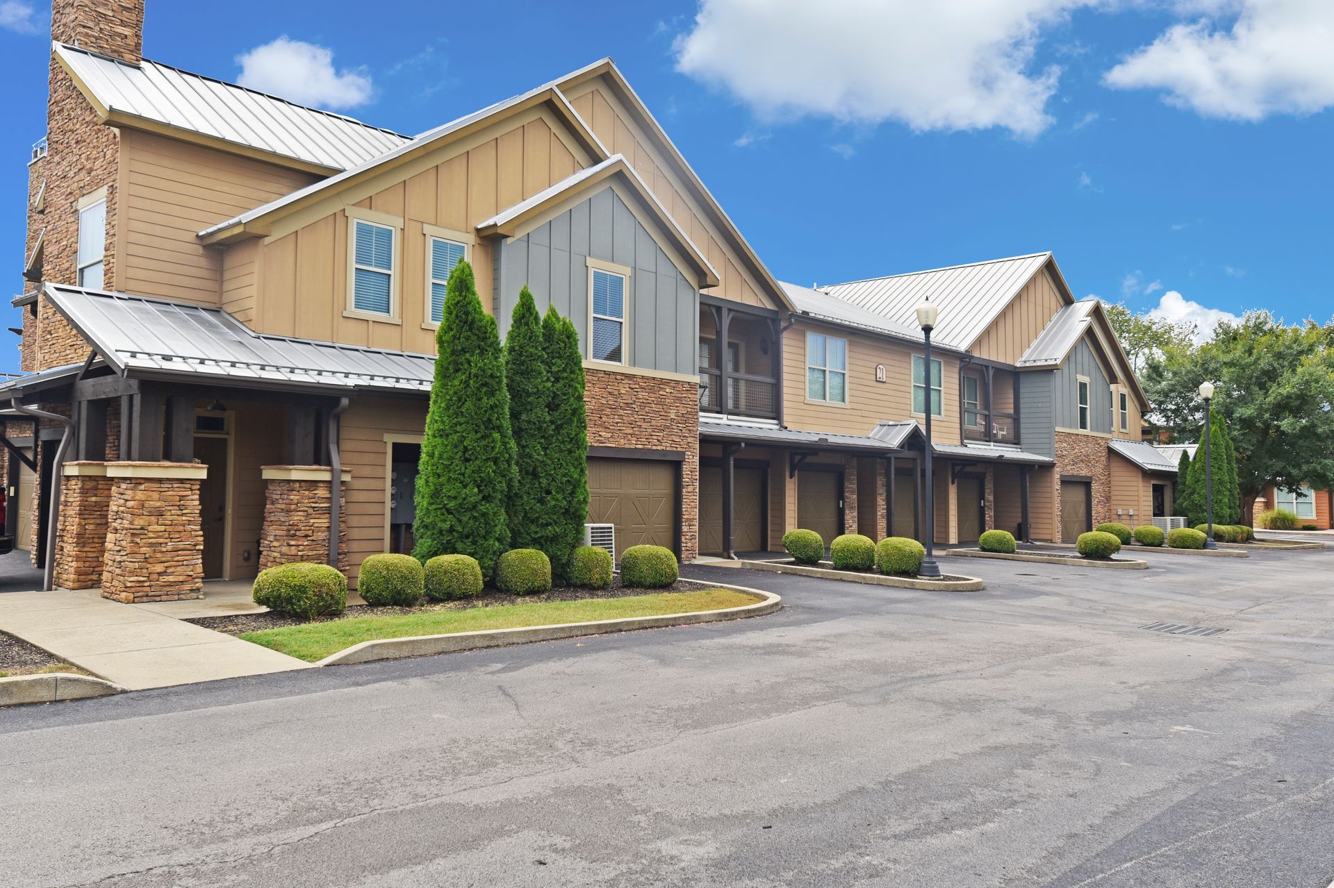 Row of townhouses with tan siding, stone accents, and silver metal roofs. Blue sky above.