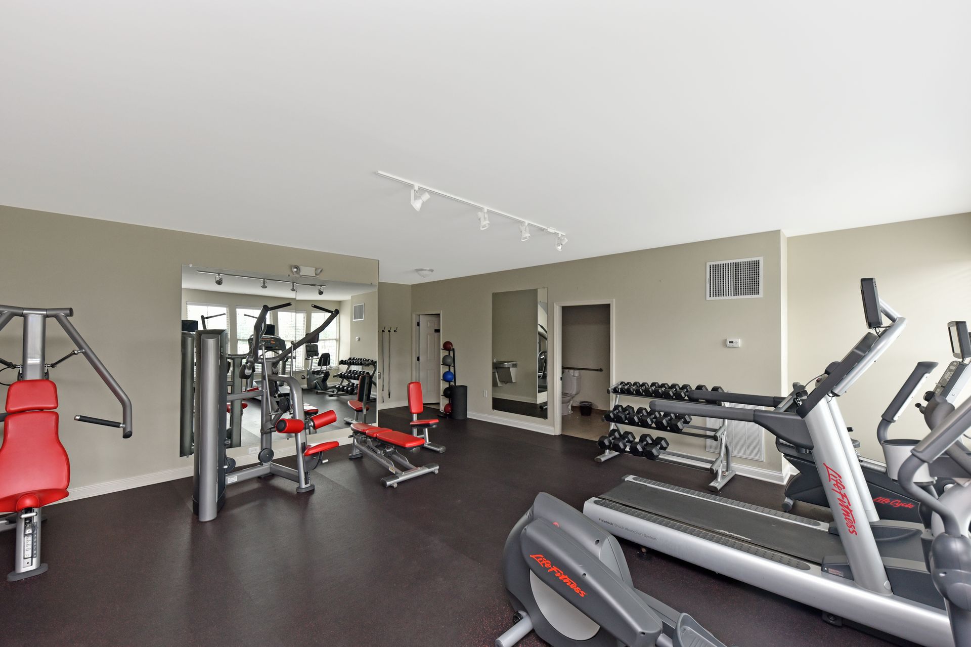 Gym with various exercise machines, free weights, and a treadmill on a dark floor.
