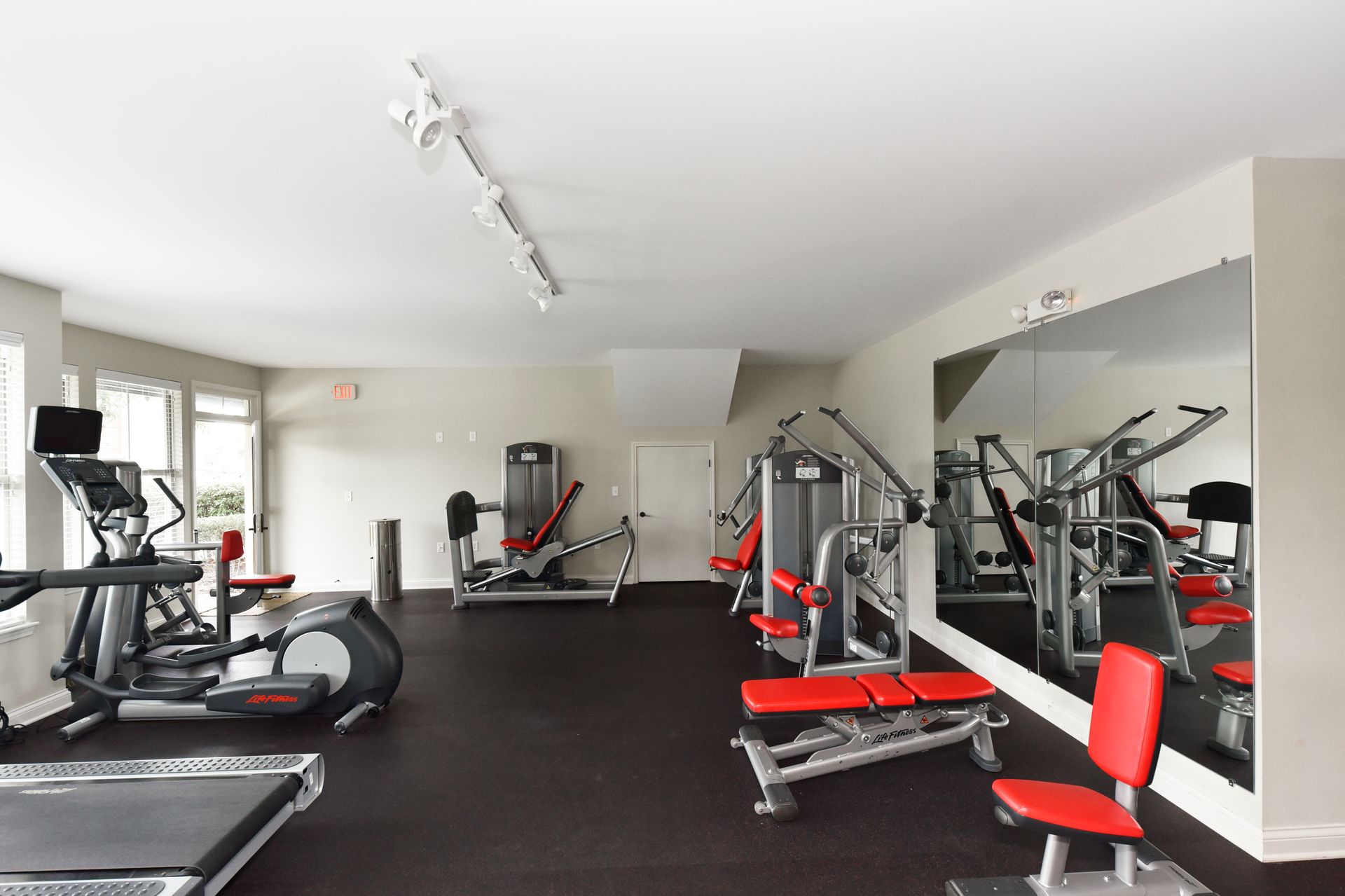 Gym with exercise machines, mirrors, and dark flooring.